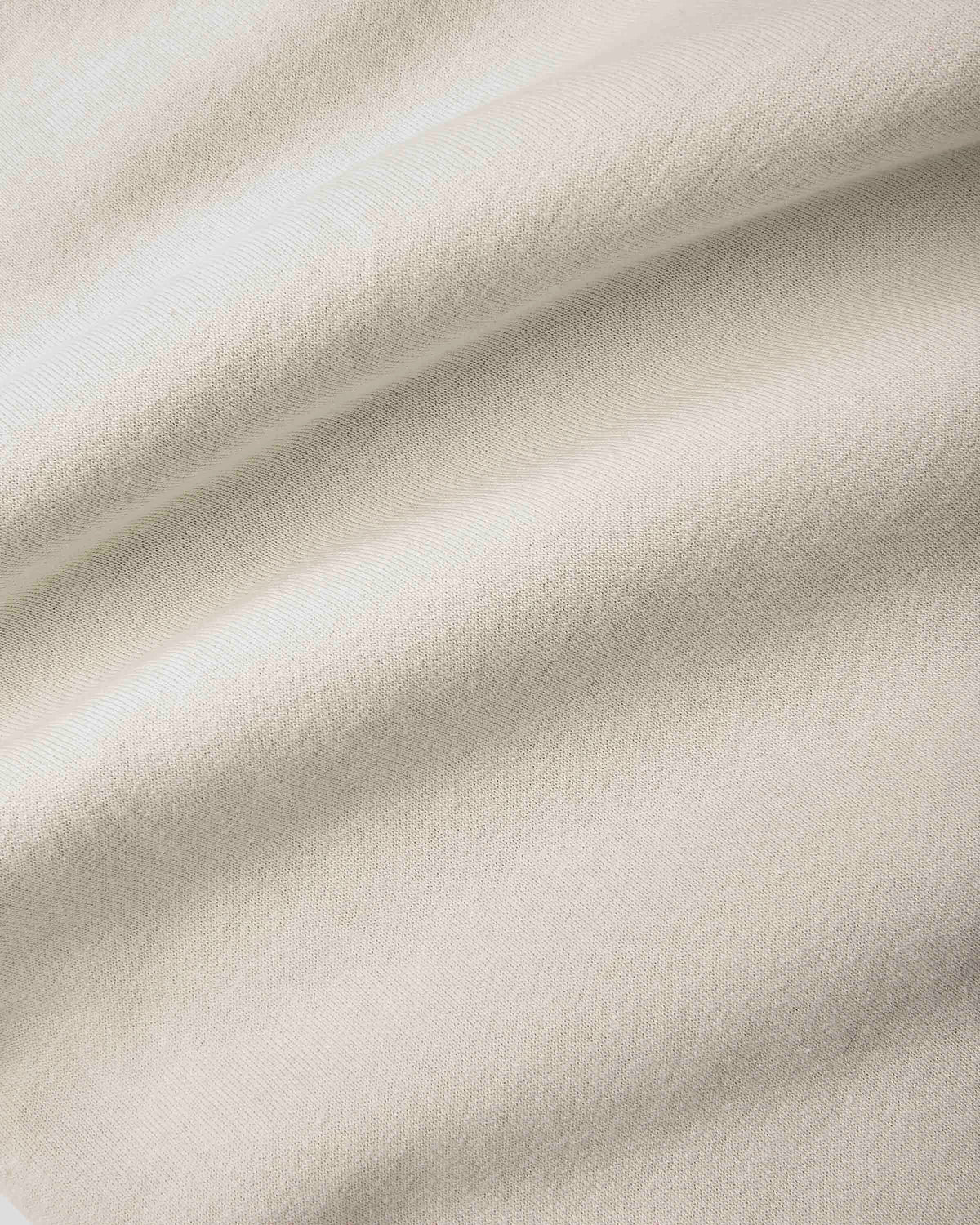 A close-up of draped off-white fabric with soft folds and a fine woven texture.
