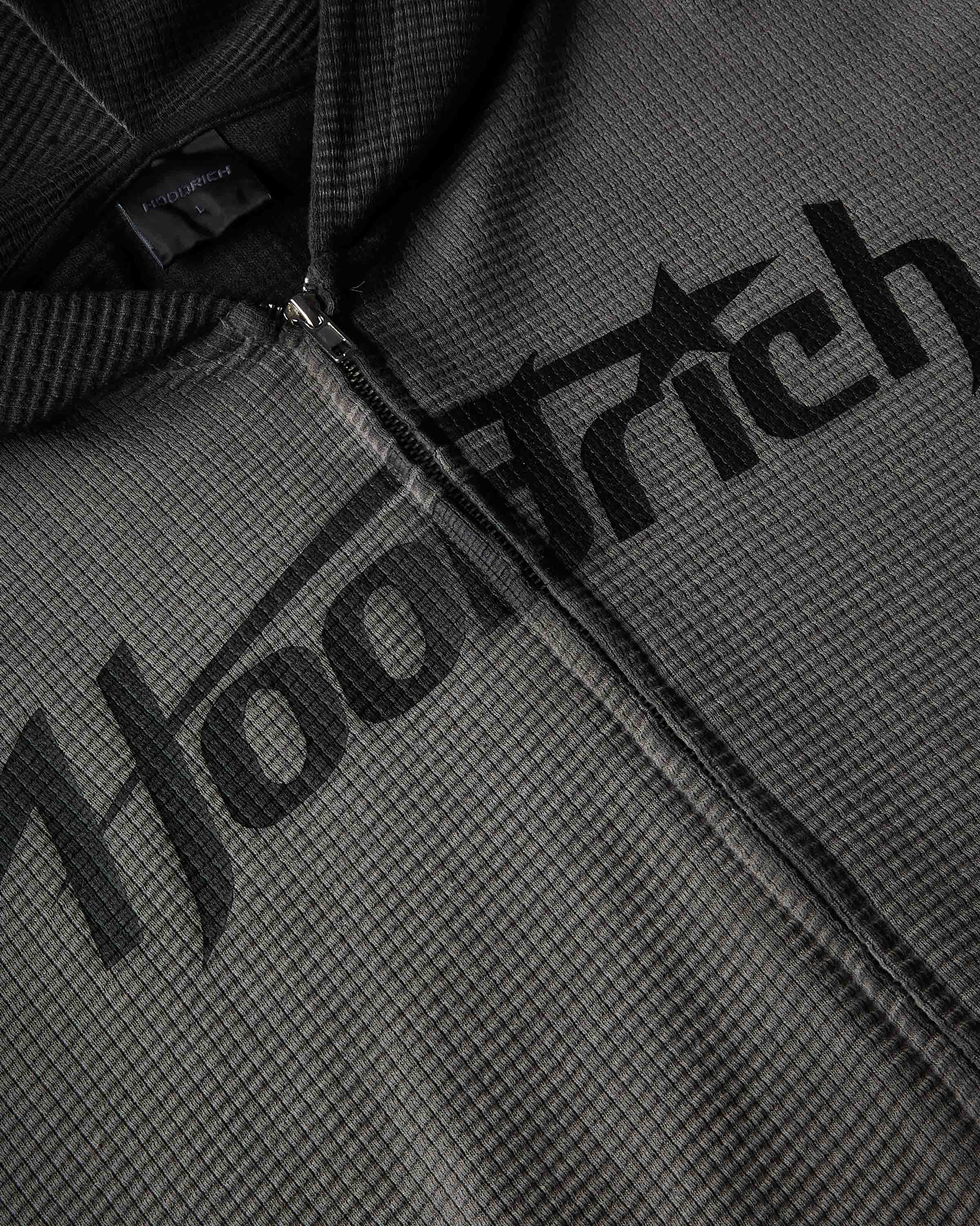 Close-up of a dark gray waffle-knit zip-up hoodie with a large black 'Hoodrich' logo printed across the chest.