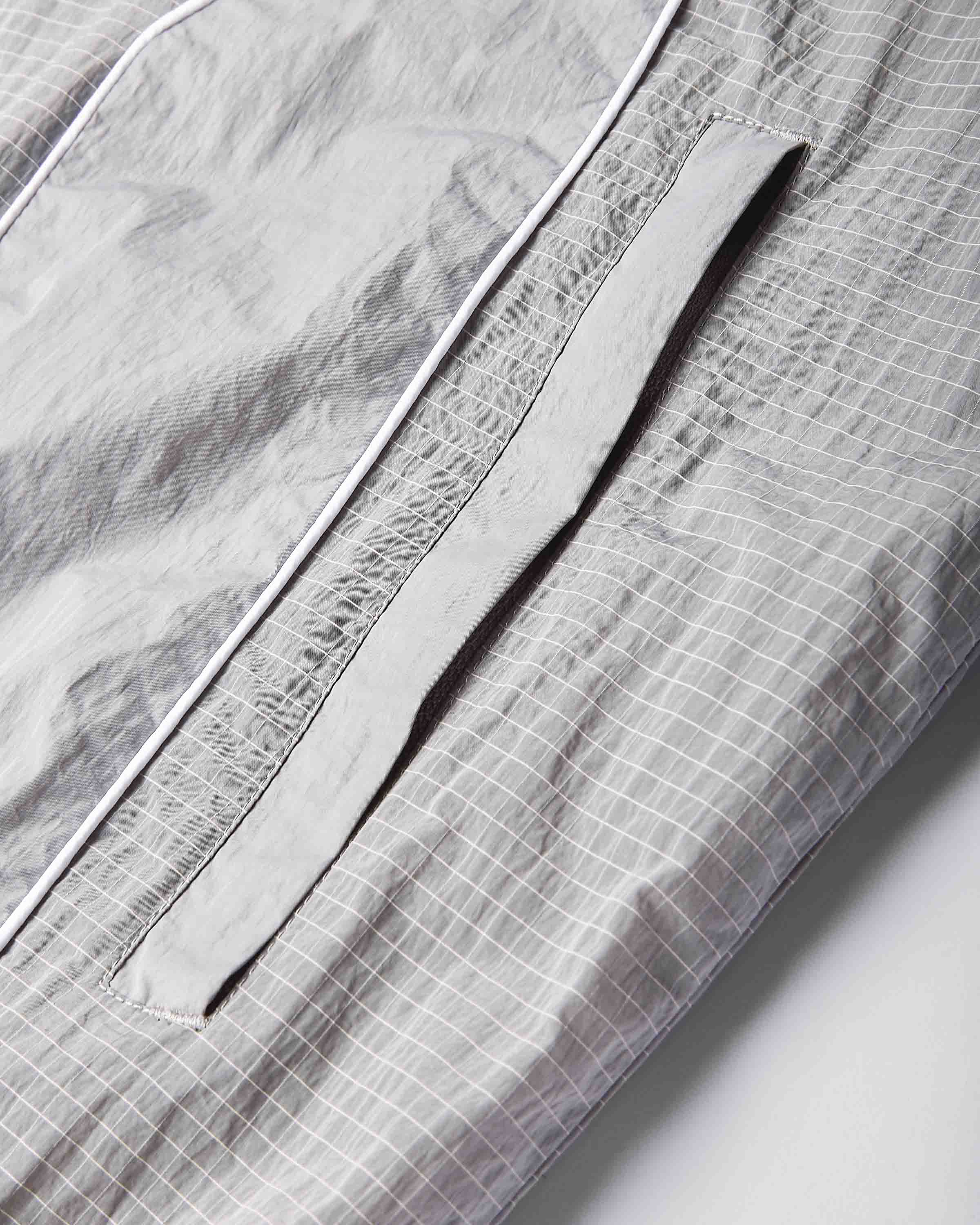Close-up of a light gray and white checkered fabric garment, showing a pocket with a matching gray flap and white piping.