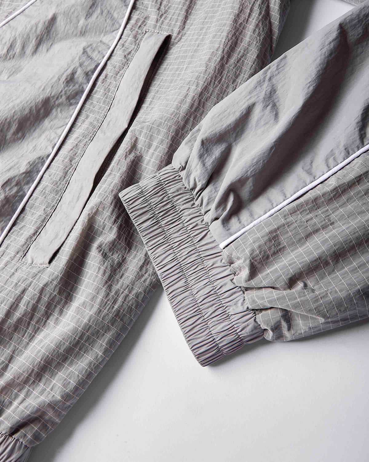 Close-up of a light gray and white checkered lounge set, showing the elasticized cuff of one sleeve and a matching drawstring detail on the other piece.