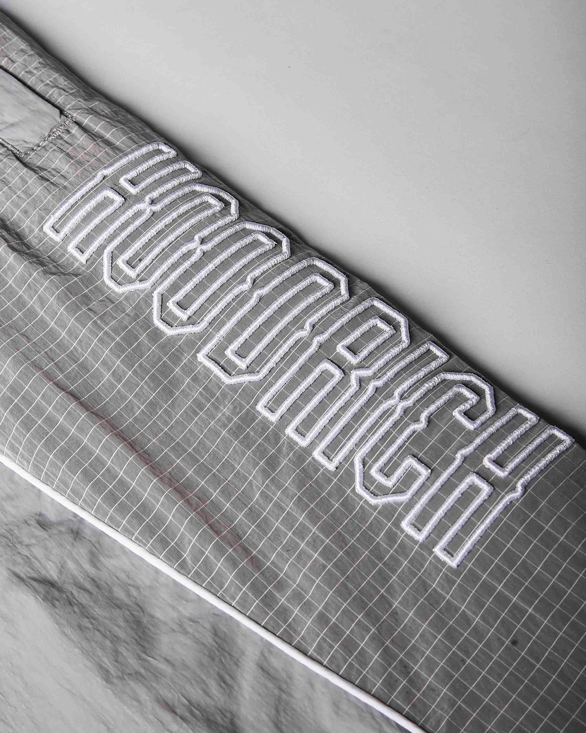 Close-up of a gray grid-patterned fabric item, likely a blanket or comforter, featuring large white varsity-style outlined lettering that reads 'HOODRICH'.