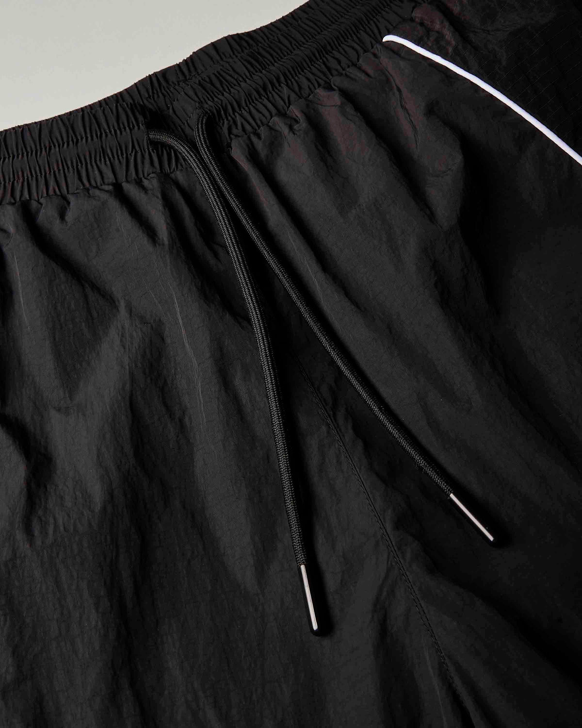Close-up of black drawstring shorts with a white piping accent near the waistband.