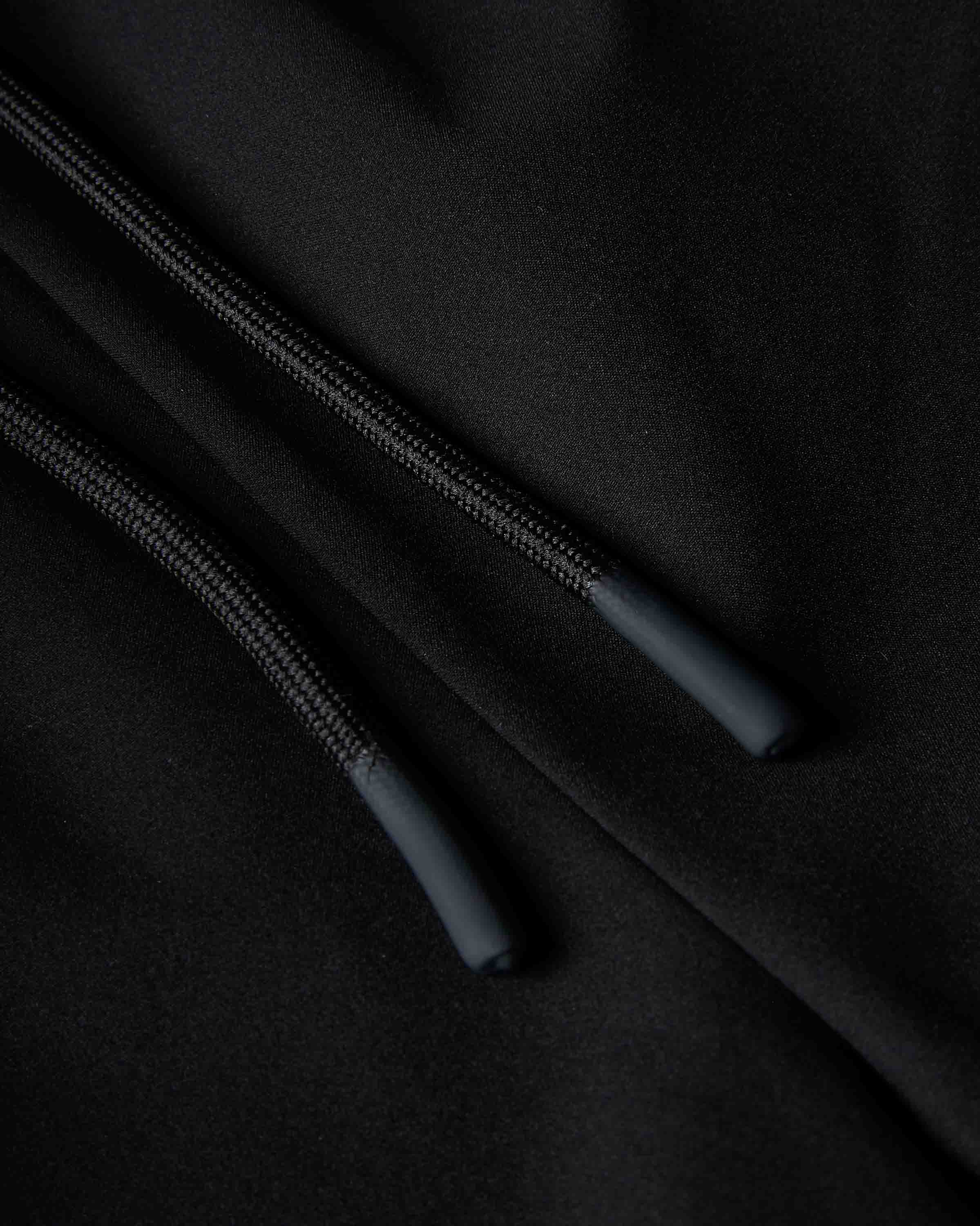 Close-up of a black hoodie showing the drawstring cords and ribbed fabric texture.