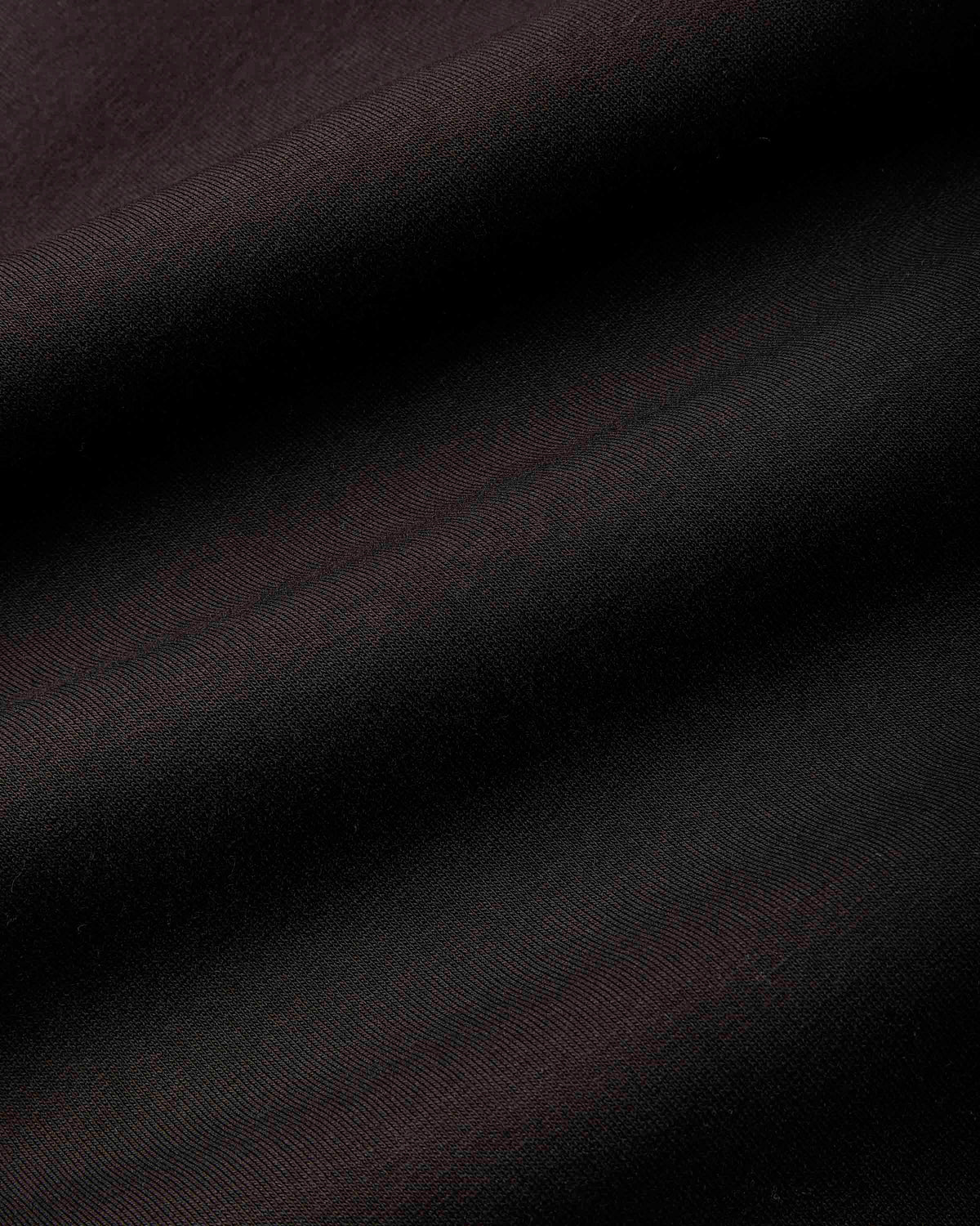 A close-up of dark fabric with a subtle sheen, showing diagonal folds and a fine woven texture in very dark brown or near-black tones.