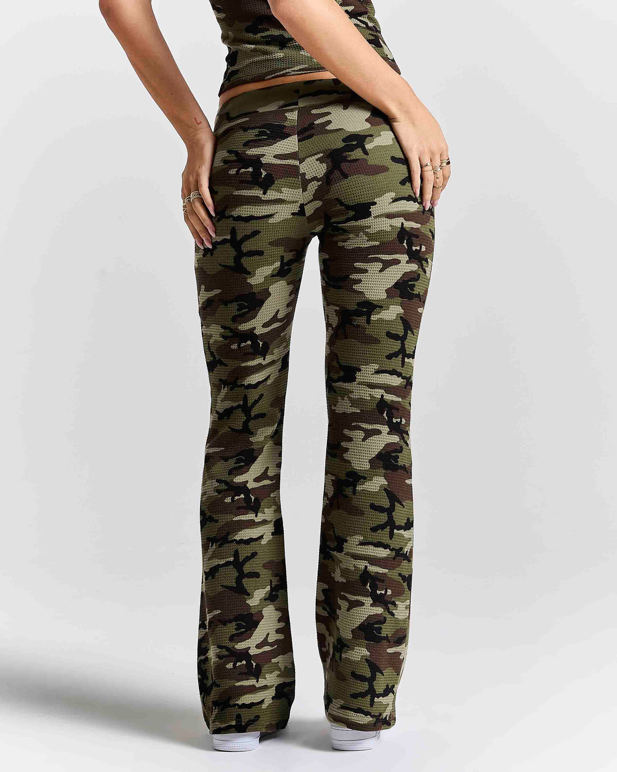A person shown from the back wearing camouflage pants with a straight-to-flare leg, paired with a matching camouflage top against a light gray studio background.