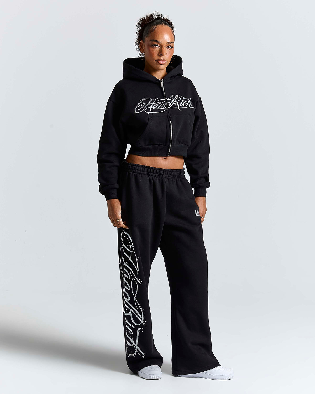 Displays a model wearing the Black 'Hoodrich' branded women's Solace Full Tracksuit