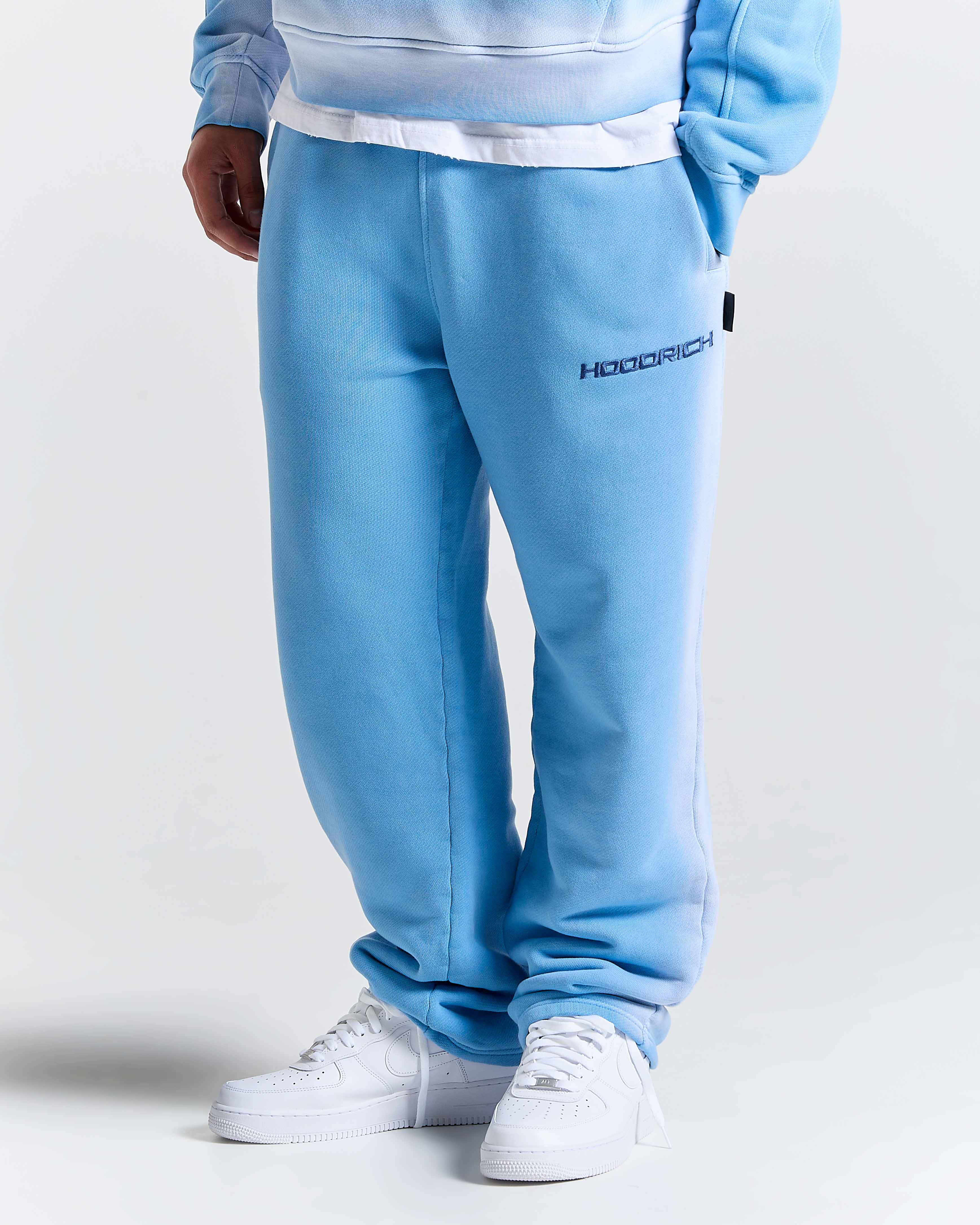 Model wearing oversized blue joggers with a black Hoodrich logo embroidery on the thigh.