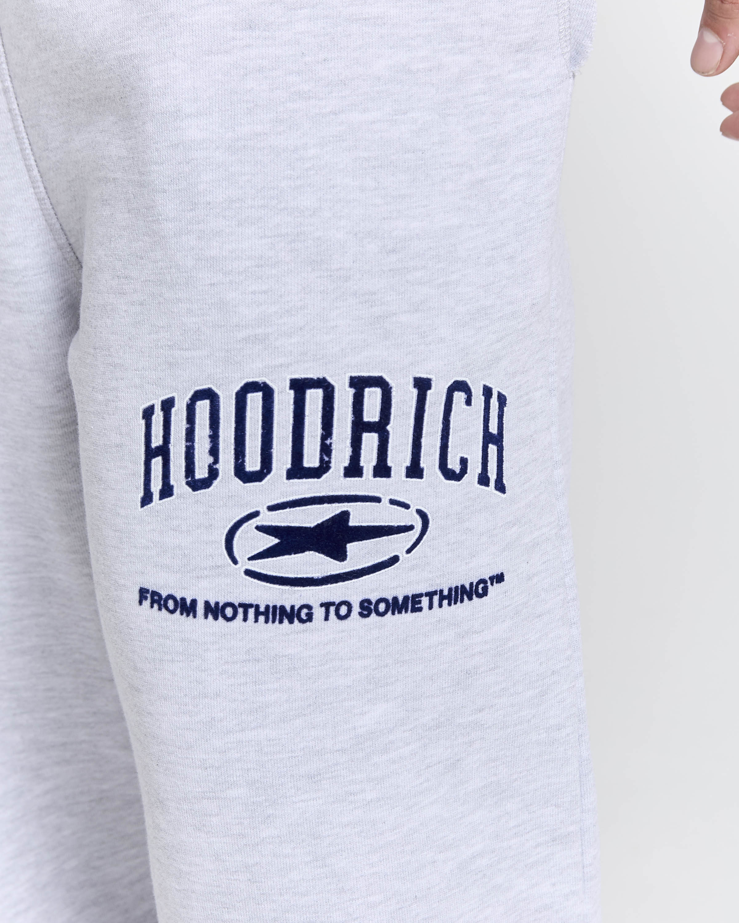 Close-up of a light heather gray sweatshirt with a navy blue 'HOODRICH' graphic and the slogan 'FROM NOTHING TO SOMETHING' on the front.