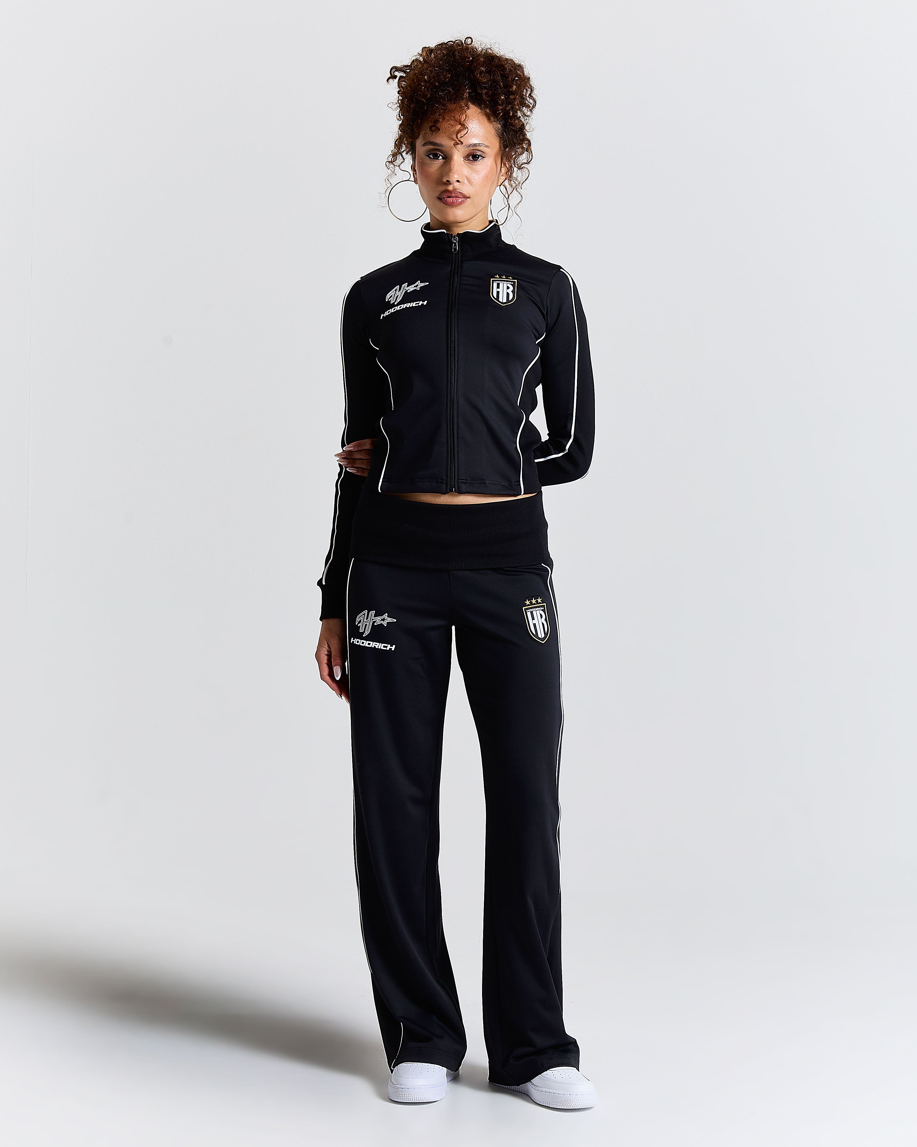 Woman wearing a black tracksuit with logos on a light gray background