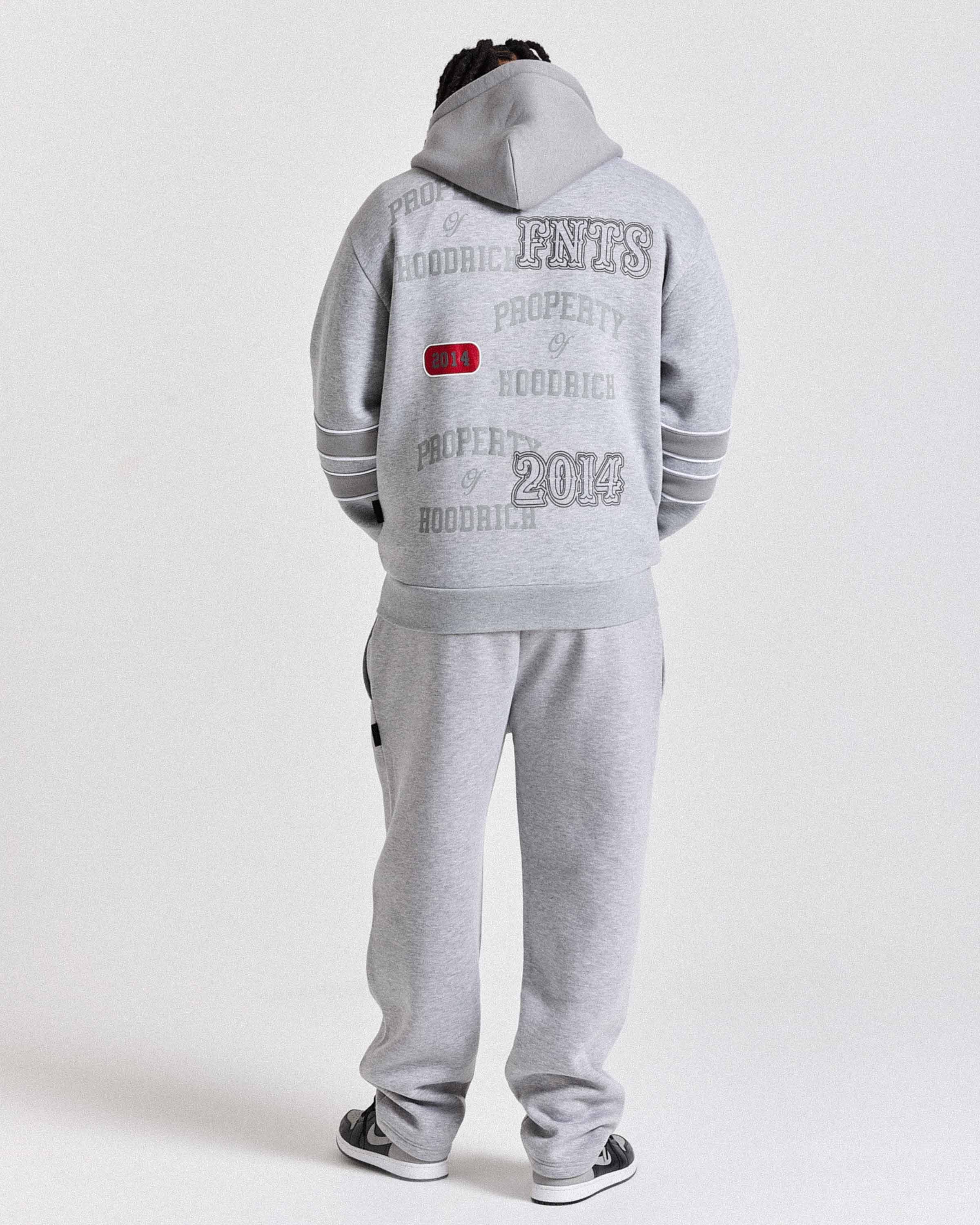 Person wearing a gray tracksuit with text on the back against a white background