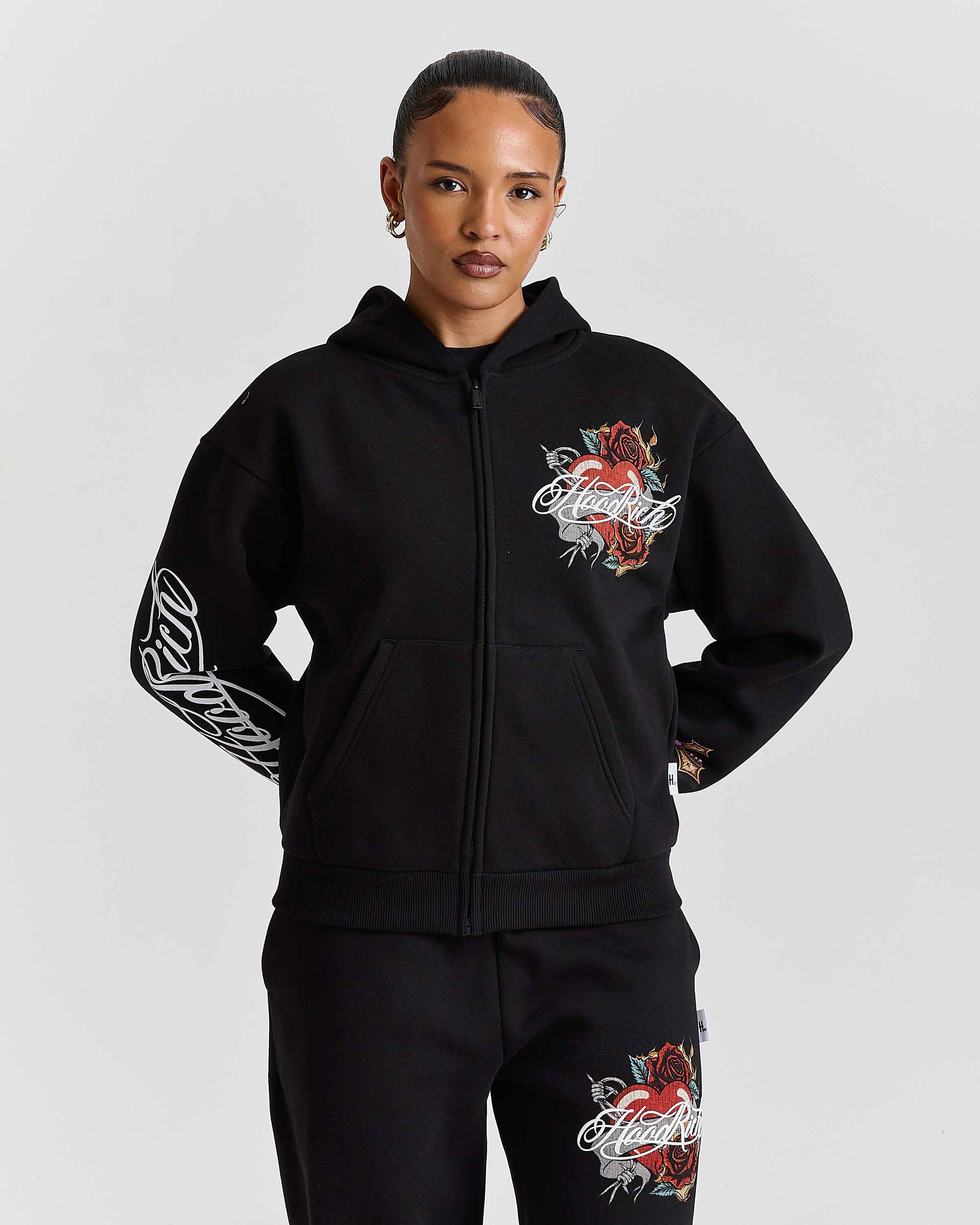 Person wearing a black hoodie and pants with floral designs and text on a plain background