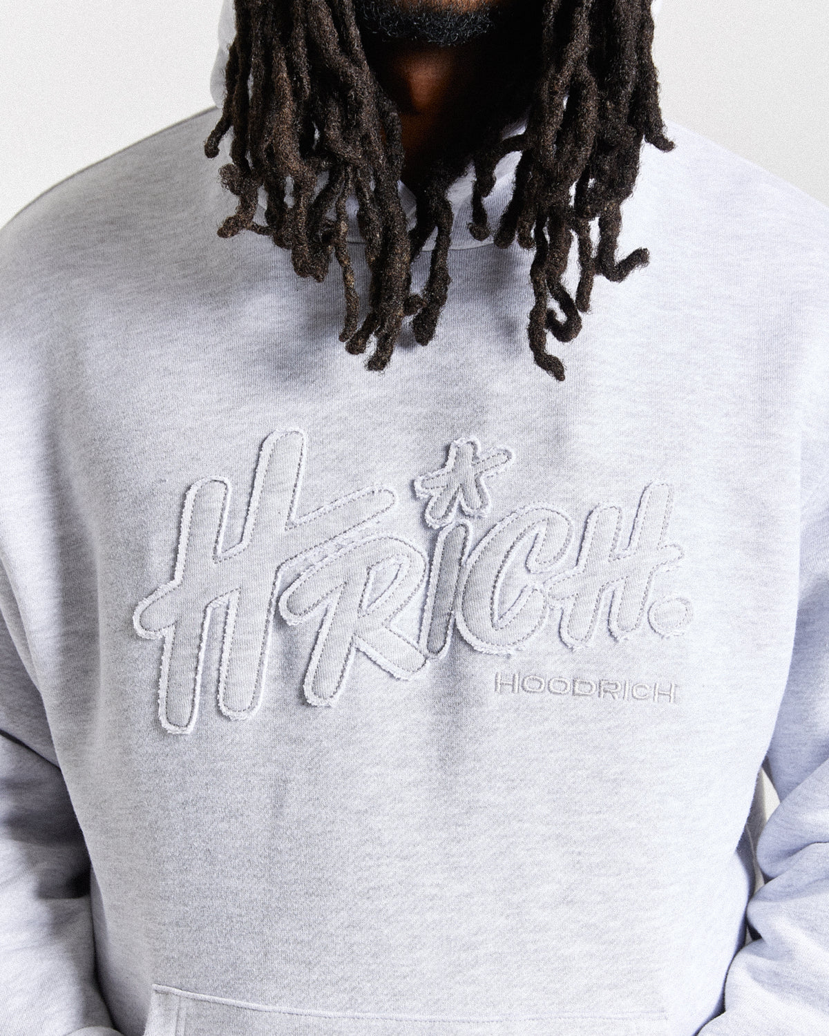 Displays a model wearing the light grey 'Hoodrich' branded men's Asthrich Full Tracksuit featuring the details on the branding
