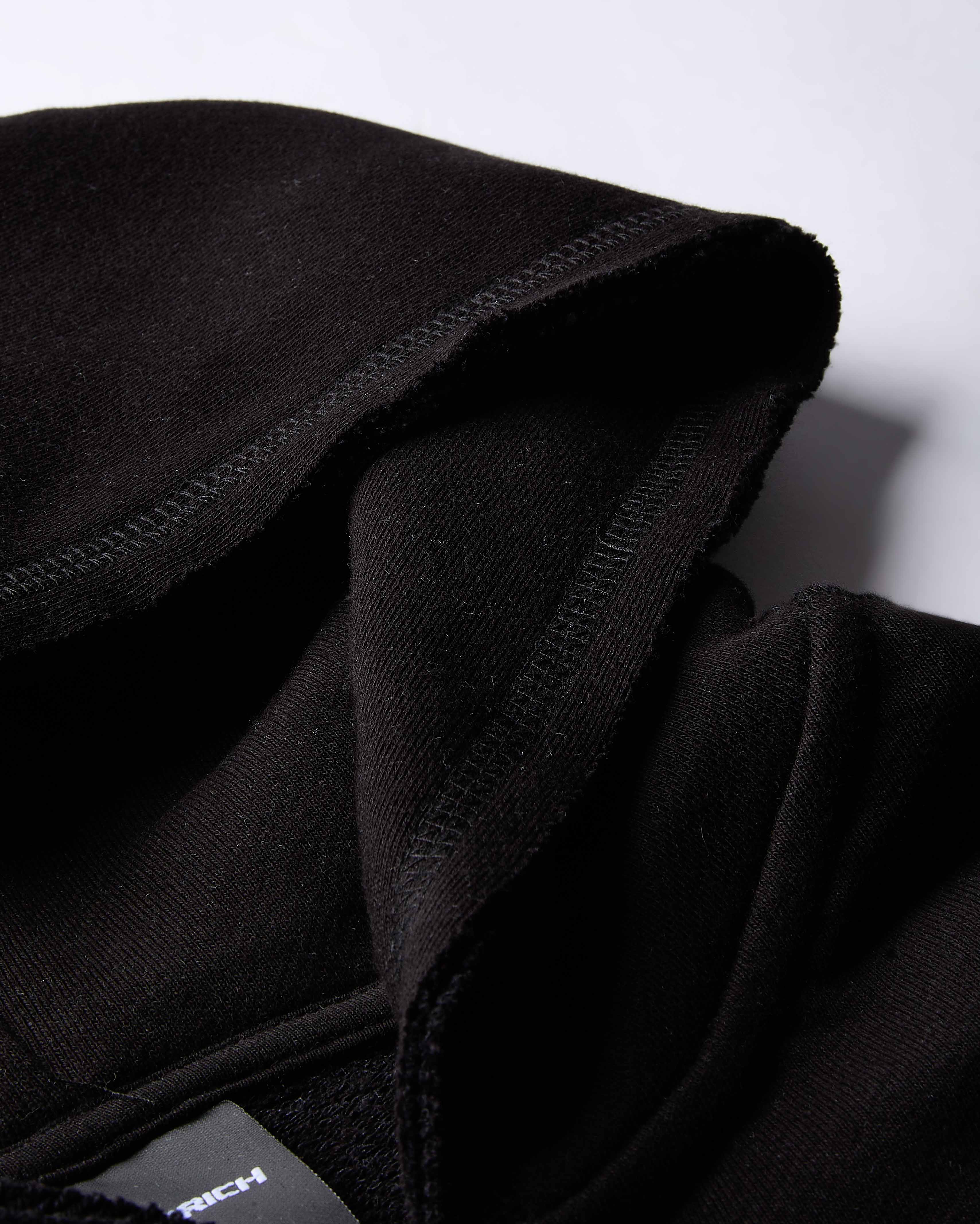 Close-up of a black fleece hoodie with a brand label on a white background