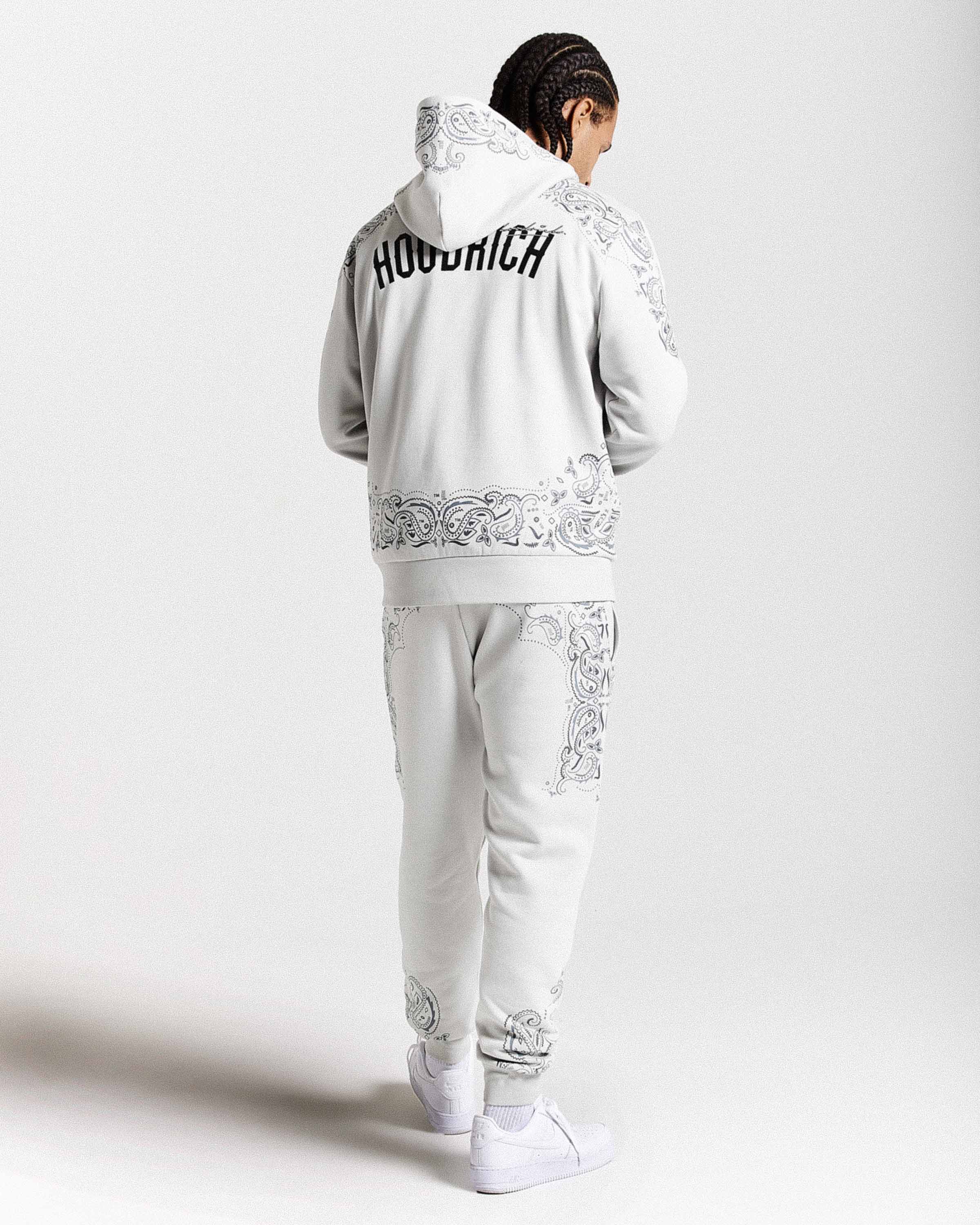 Person wearing a gray tracksuit with intricate white embroidery on a white background