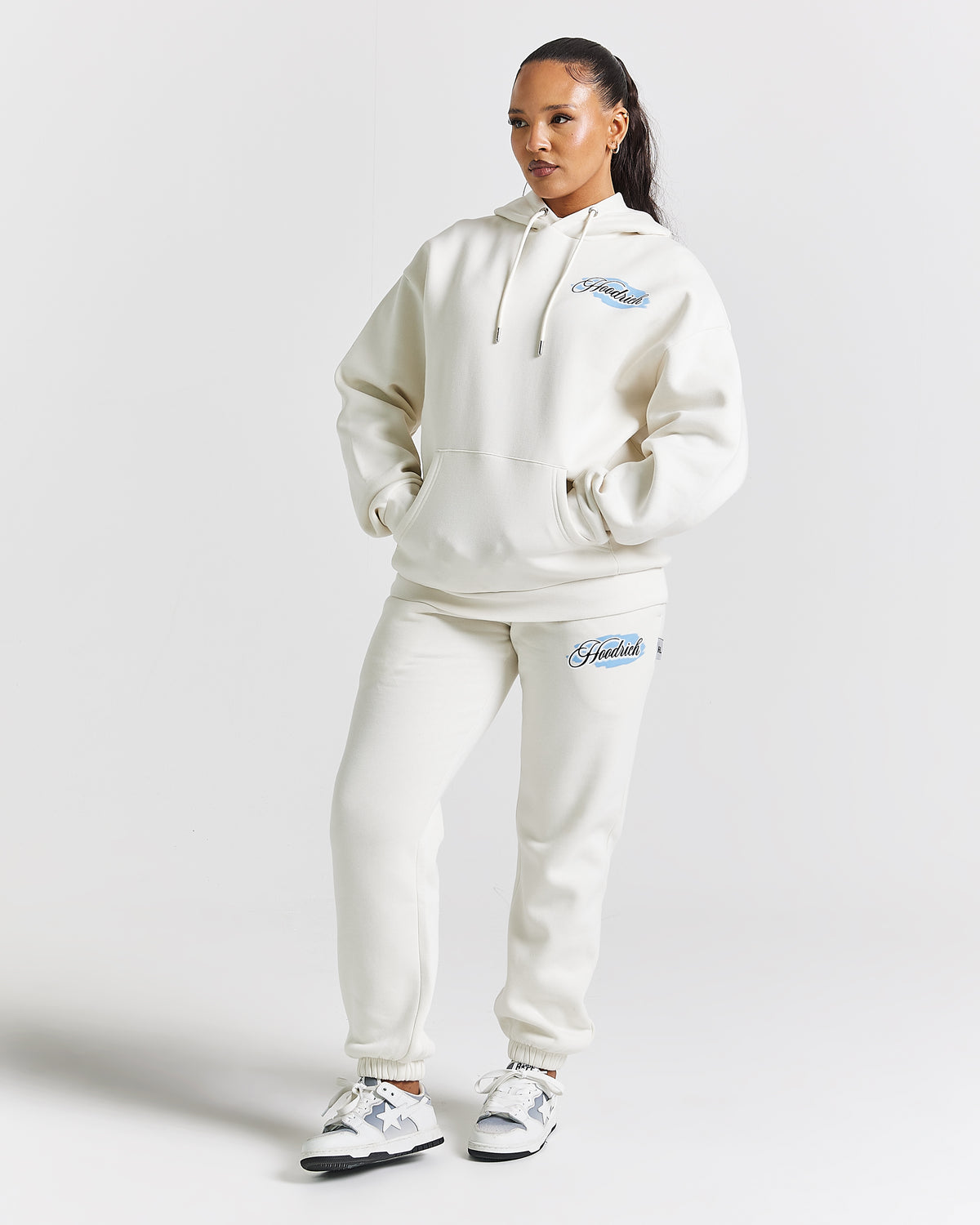 Displays a model wearing the White 'Hoodrich' branded women's Grillz Full Tracksuit
