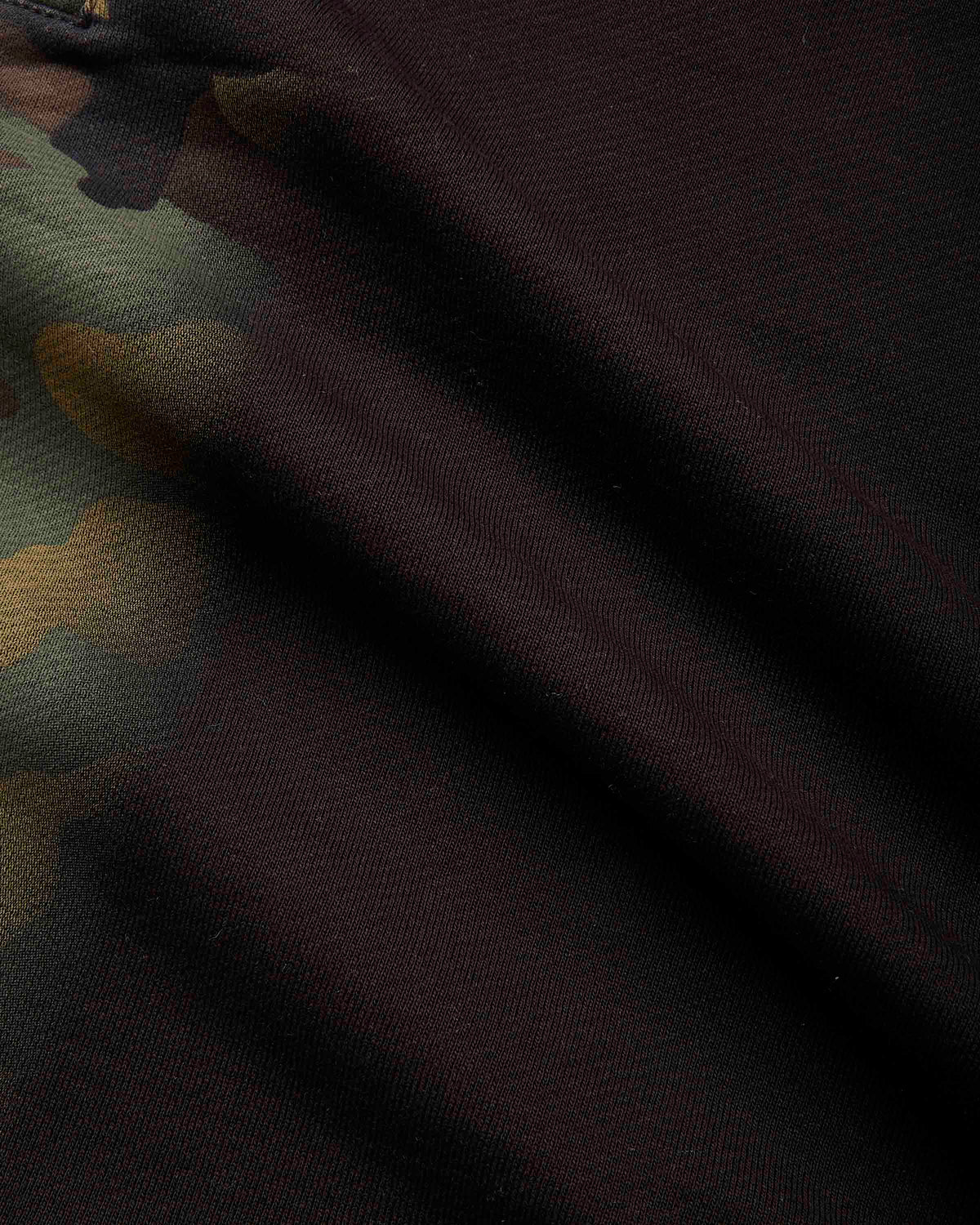 Close-up of dark camouflage fabric with a solid black or very deep charcoal section and partial olive green and tan camo areas visible on the left.