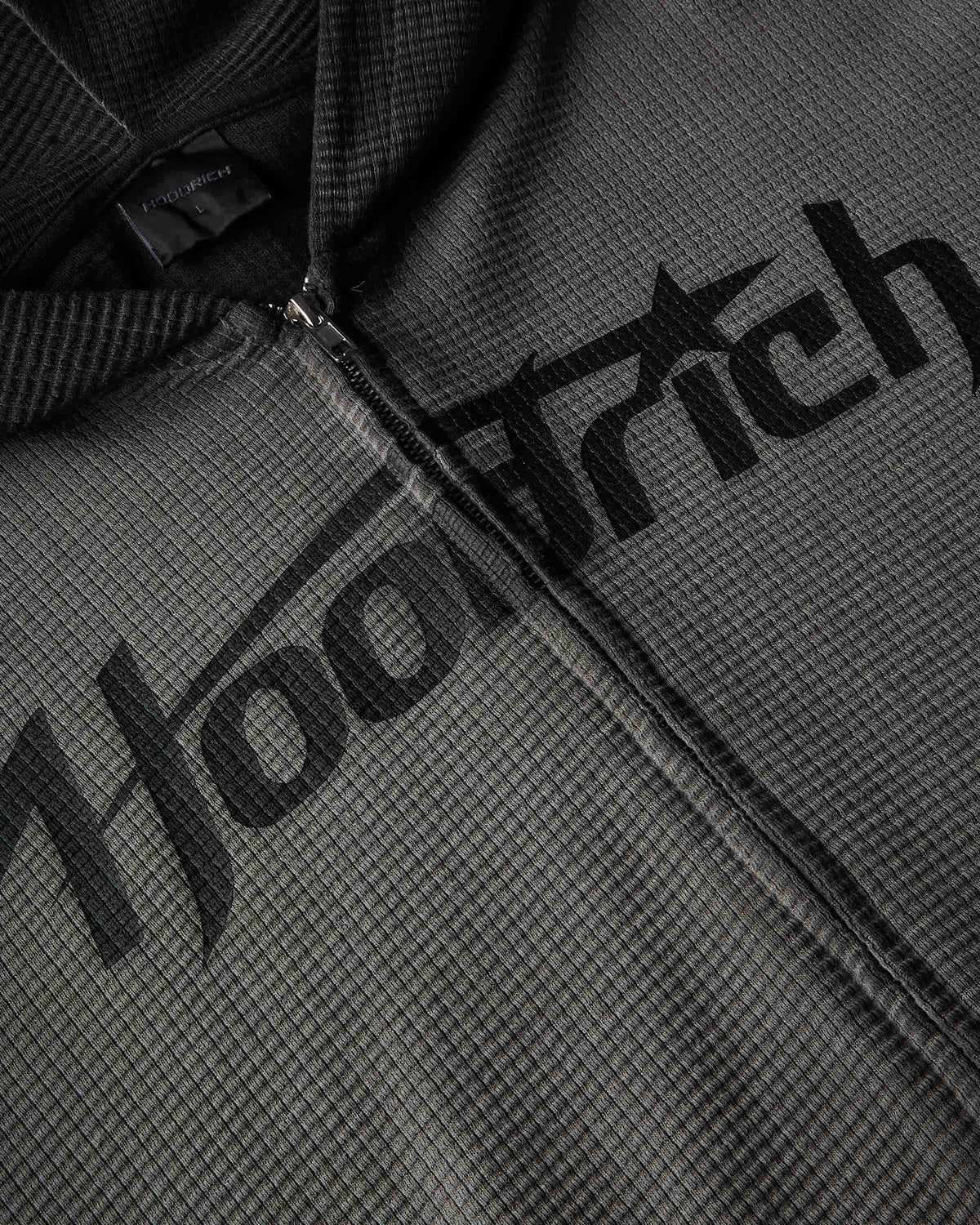 Close-up of a dark gray waffle-knit zip-up hoodie with a large black 'Hoodrich' logo printed across the chest.