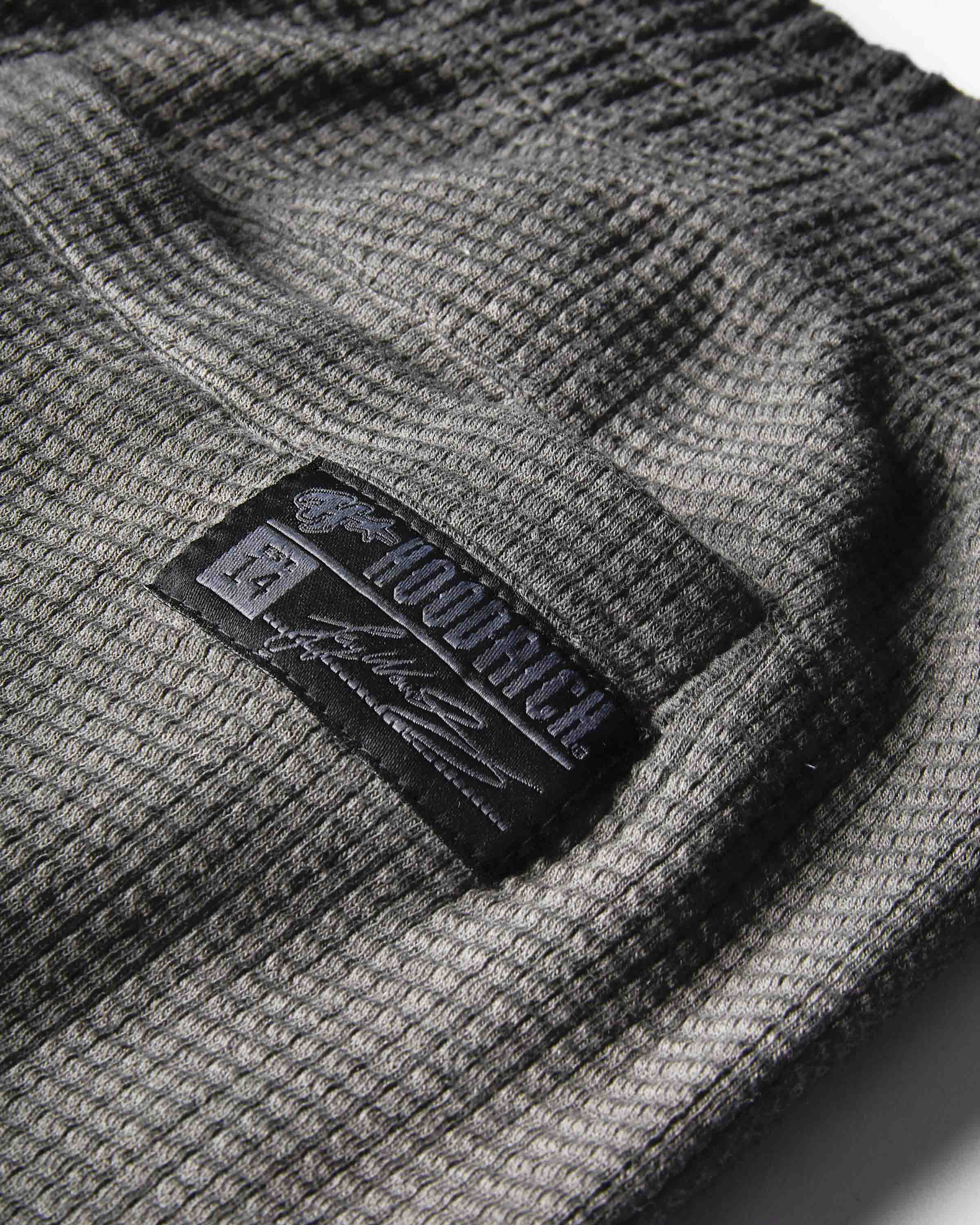 Close-up of a dark gray waffle-knit fabric with a black embroidered patch reading 'hoodrich' and on a white background.