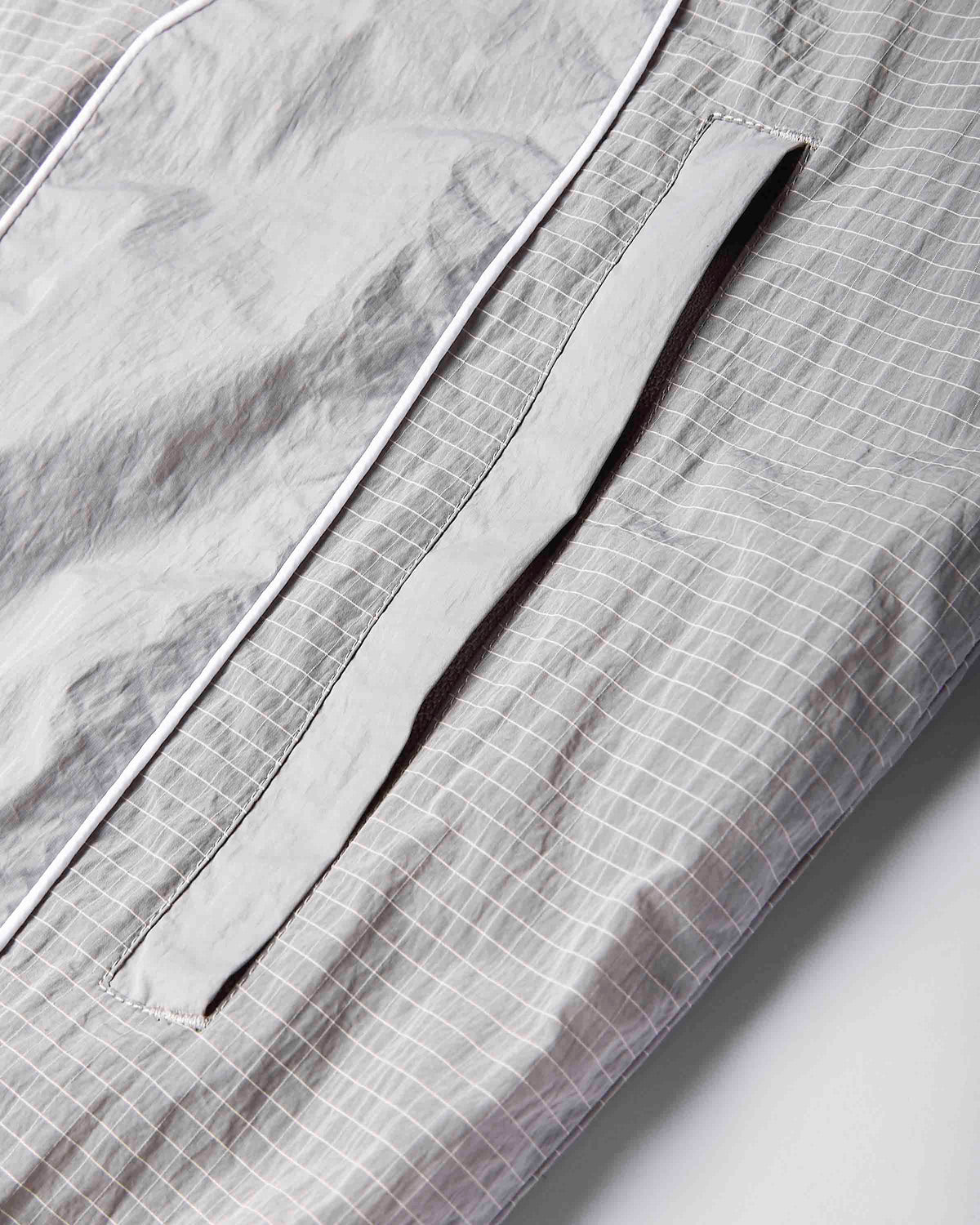 Close-up of a light gray and white checkered fabric garment, showing a pocket with a matching gray flap and white piping.
