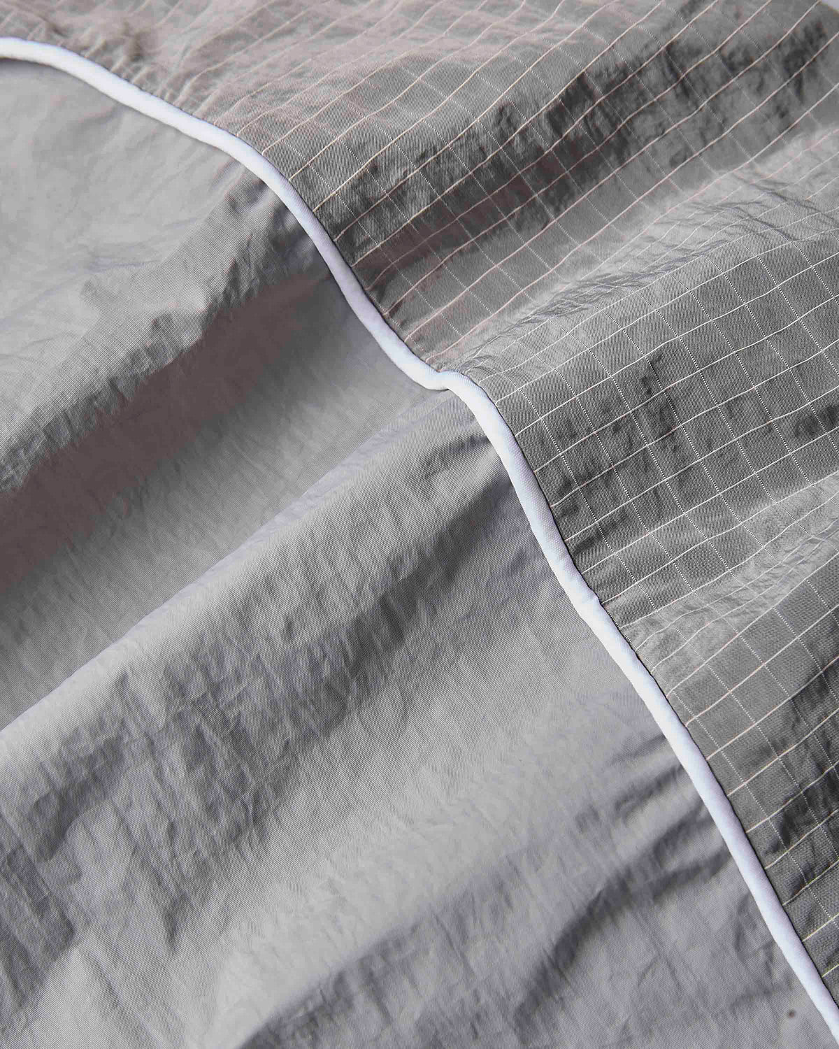 Close-up of a gray quilted fabric with a subtle grid pattern and a contrasting white piping border.