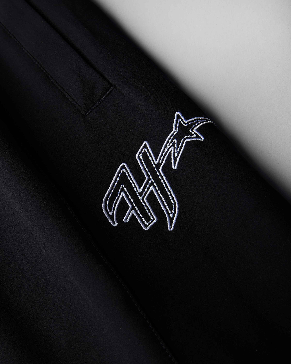 Close-up of a black garment featuring a white embroidered stylized monogram with a star on the chest.