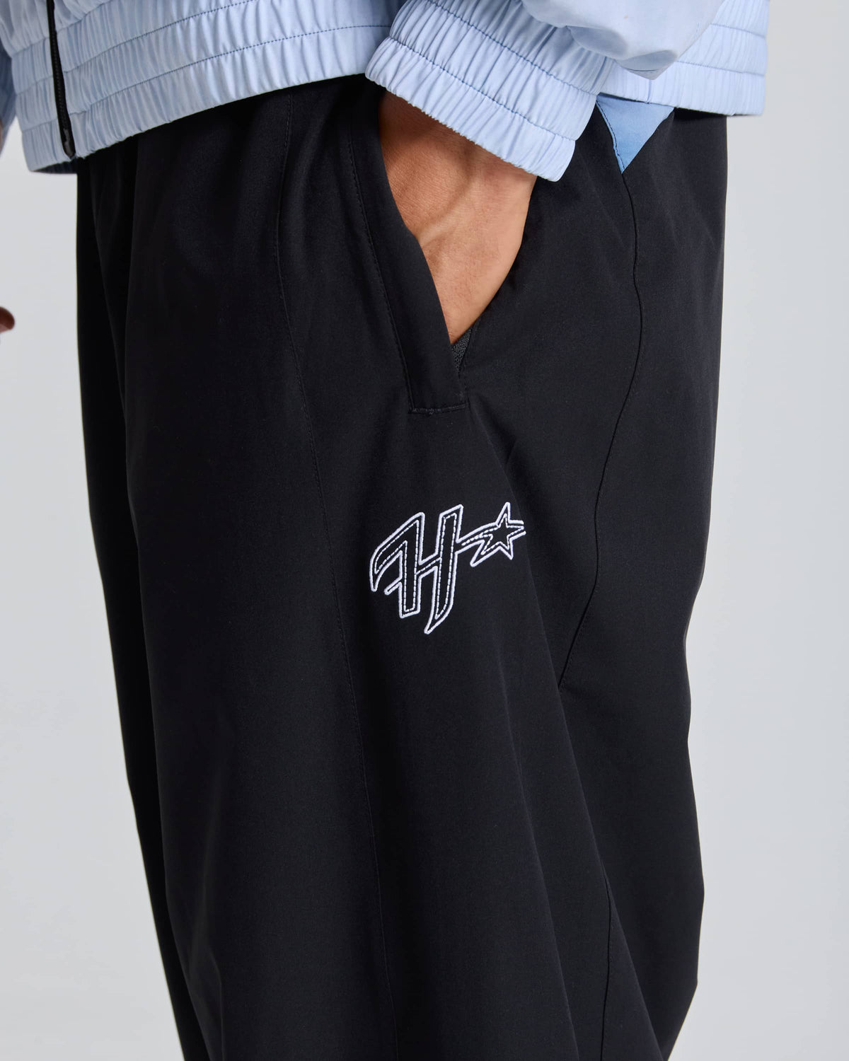 Close up of a monogram H and a star on a man wearing black pants with his hand in his pocket