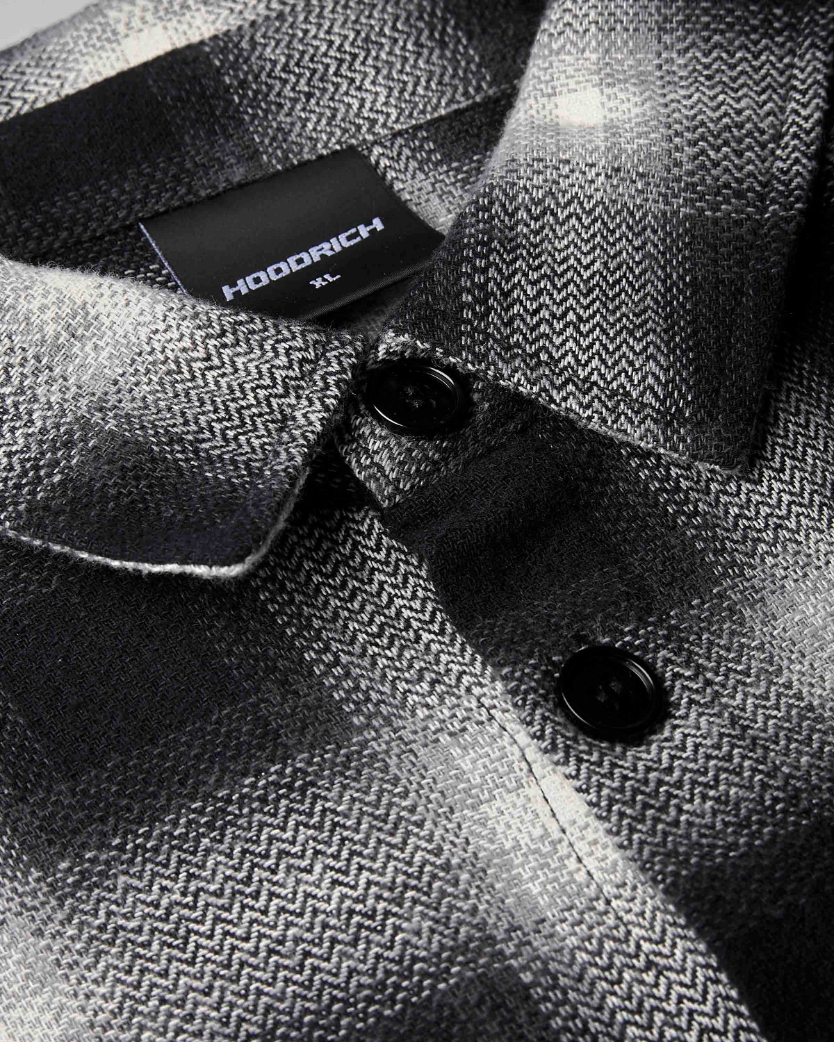 Close-up of a HODDRICH men's button-down shirt featuring a black and gray herringbone pattern, with a black brand label visible on the collar.
