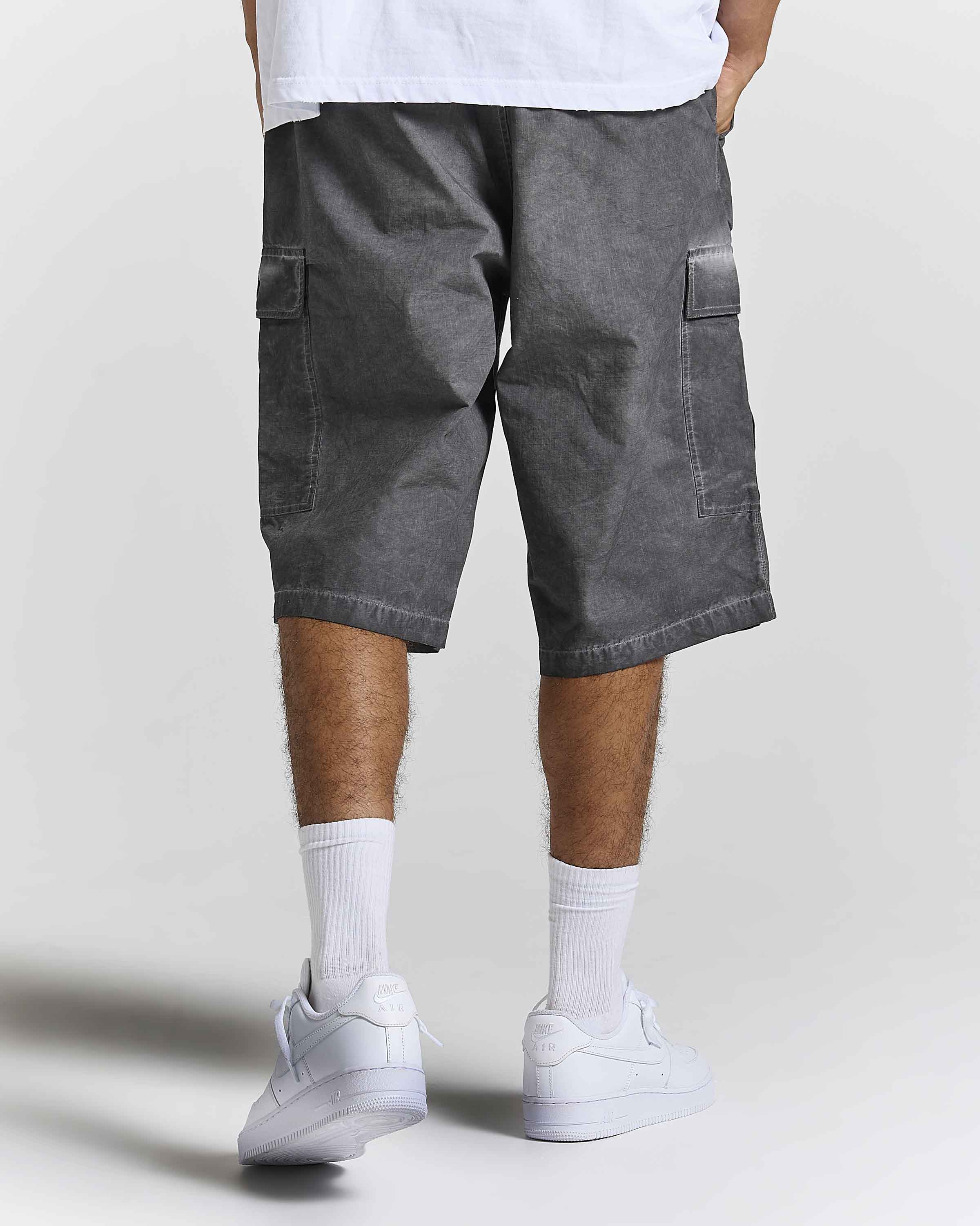 A person shown from the waist down wearing washed dark gray cargo shorts, white crew socks, and white sneakers against a light gray studio background.