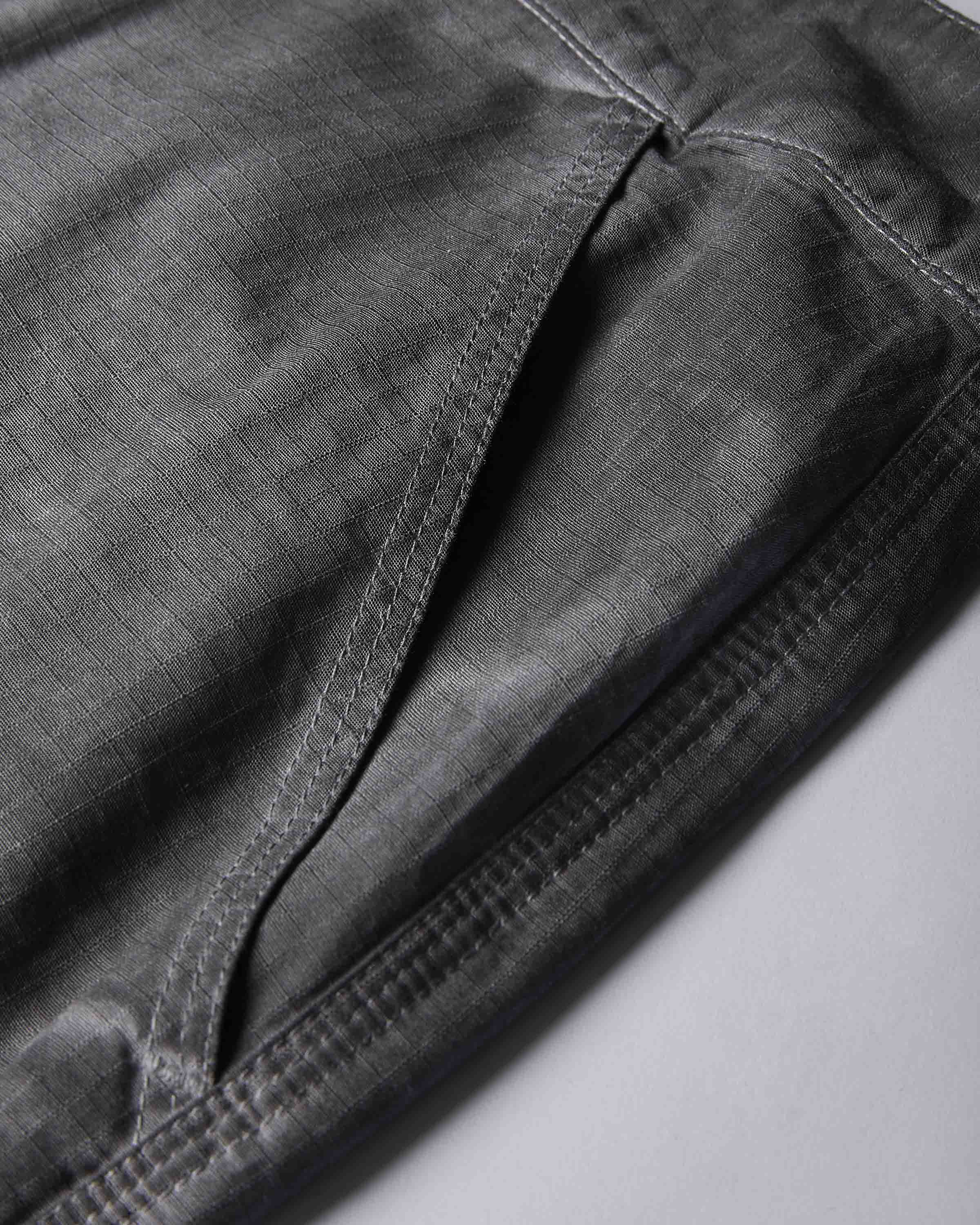 Close-up detail shot of dark gray fabric with visible stitching and texture, showing part of a garment or textile fold on a light gray background.