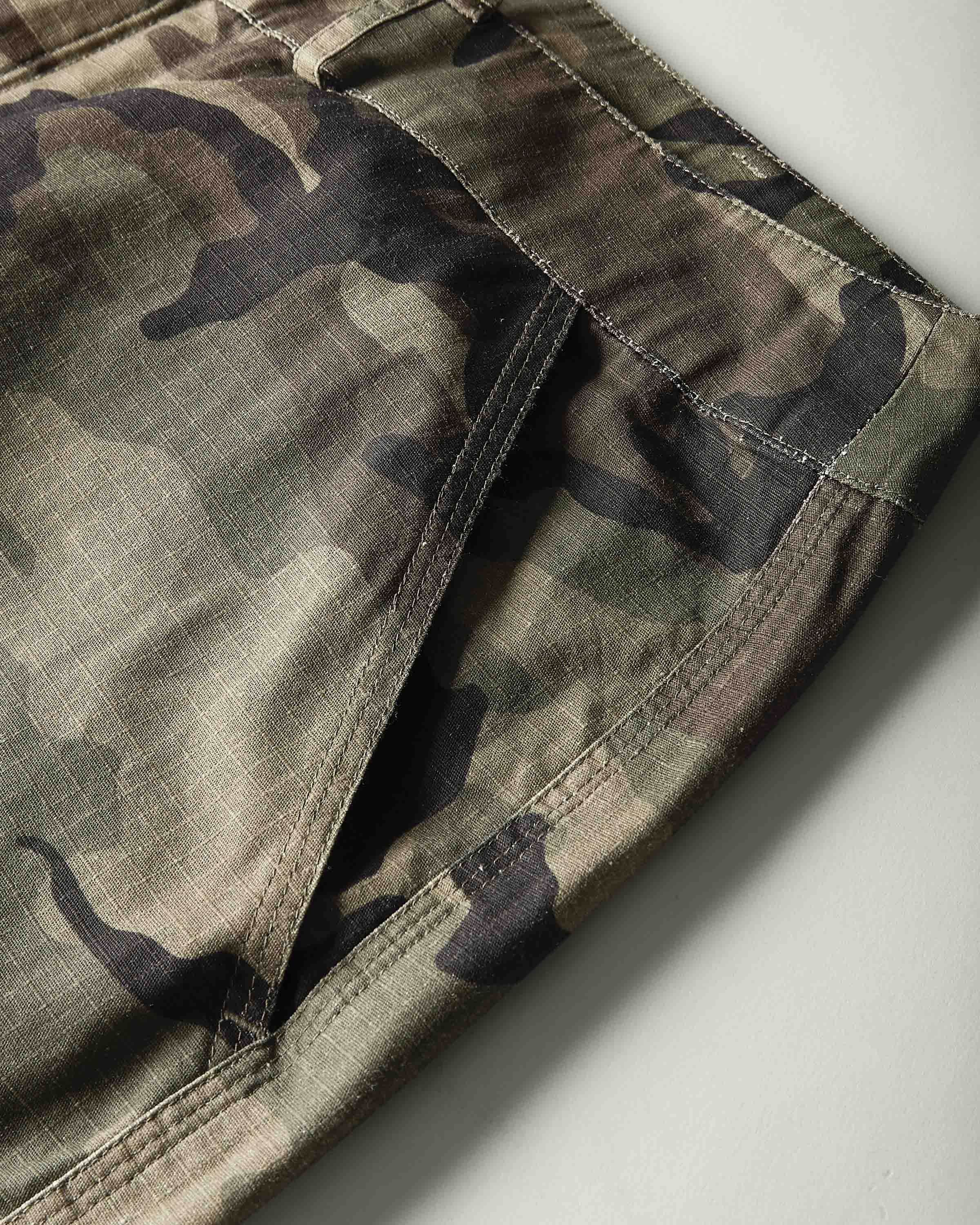 Close-up of camouflage pants showing the fabric pattern and side seam details against a light gray background.