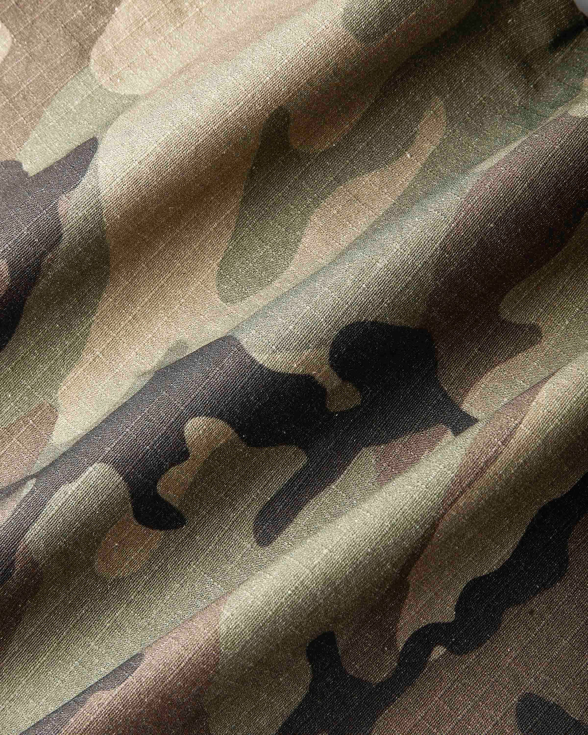 A close-up of draped camouflage fabric with a classic woodland pattern in olive green, brown, tan, and black.