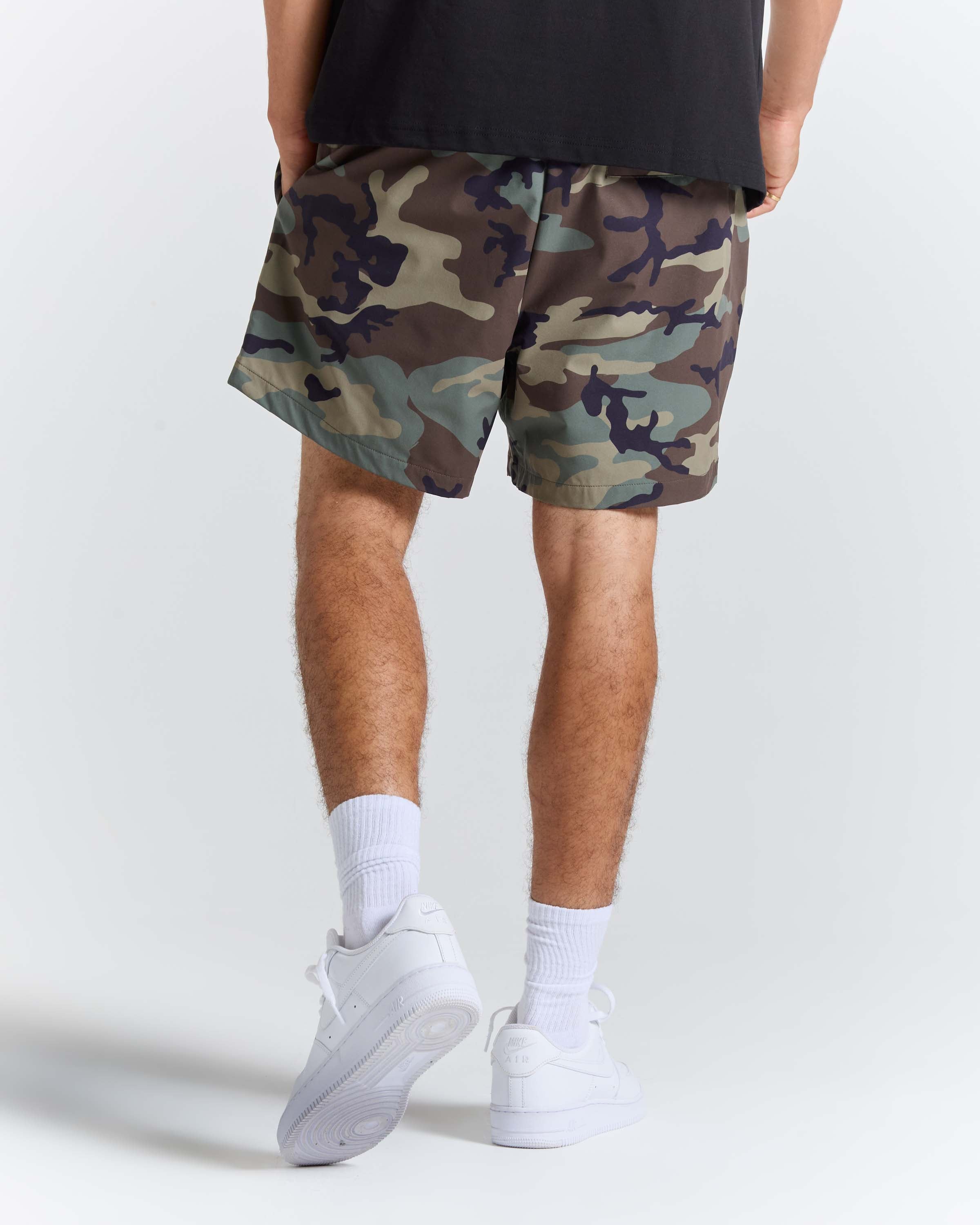 A person shown from the waist down wearing camouflage shorts, white crew socks, and white sneakers against a light gray studio background.