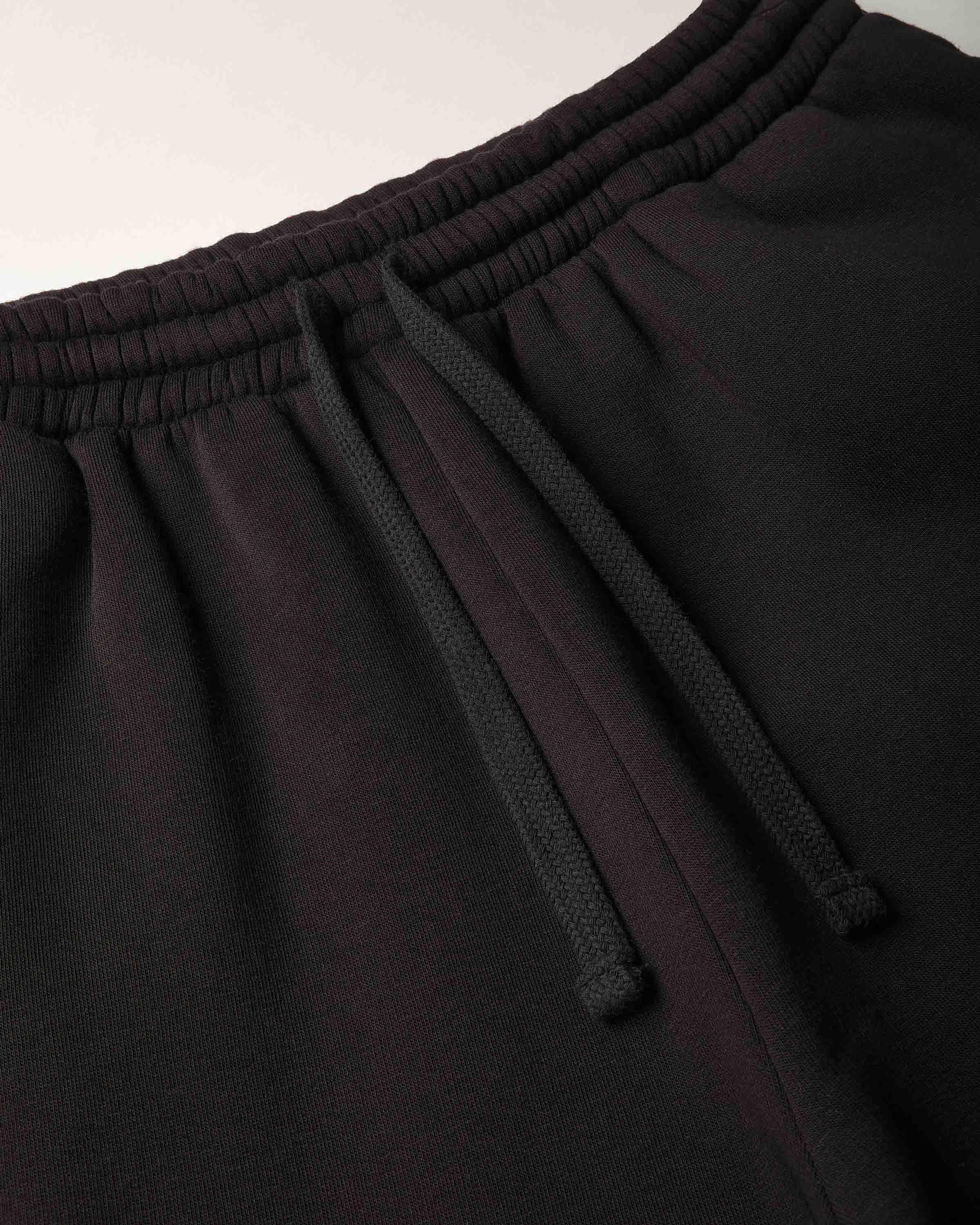 Close-up of black sweatpants showing the elastic waistband, drawstring, and fabric texture.