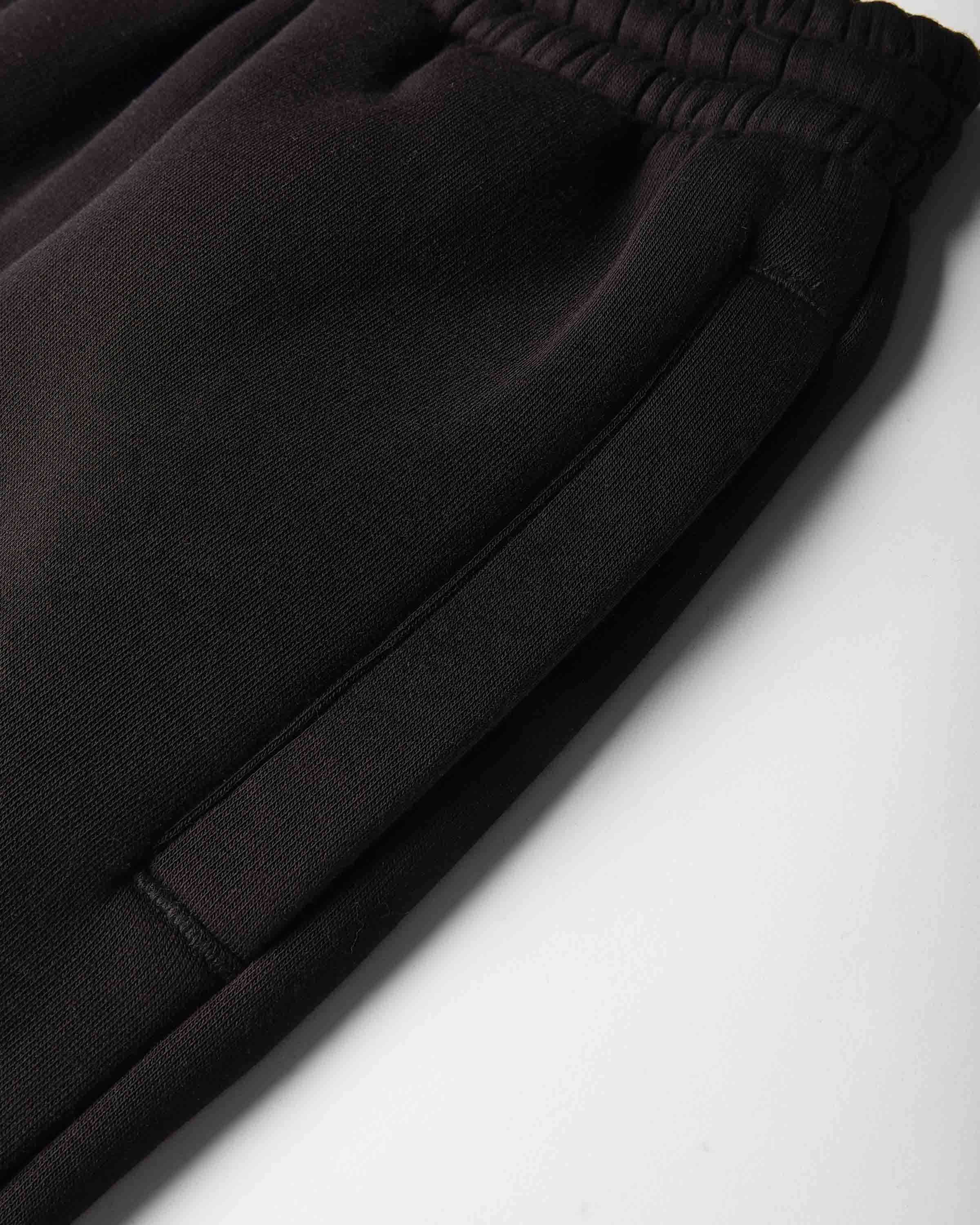 Close-up of black sweatpants showing the elastic waistband and side seam details against a light gray background.