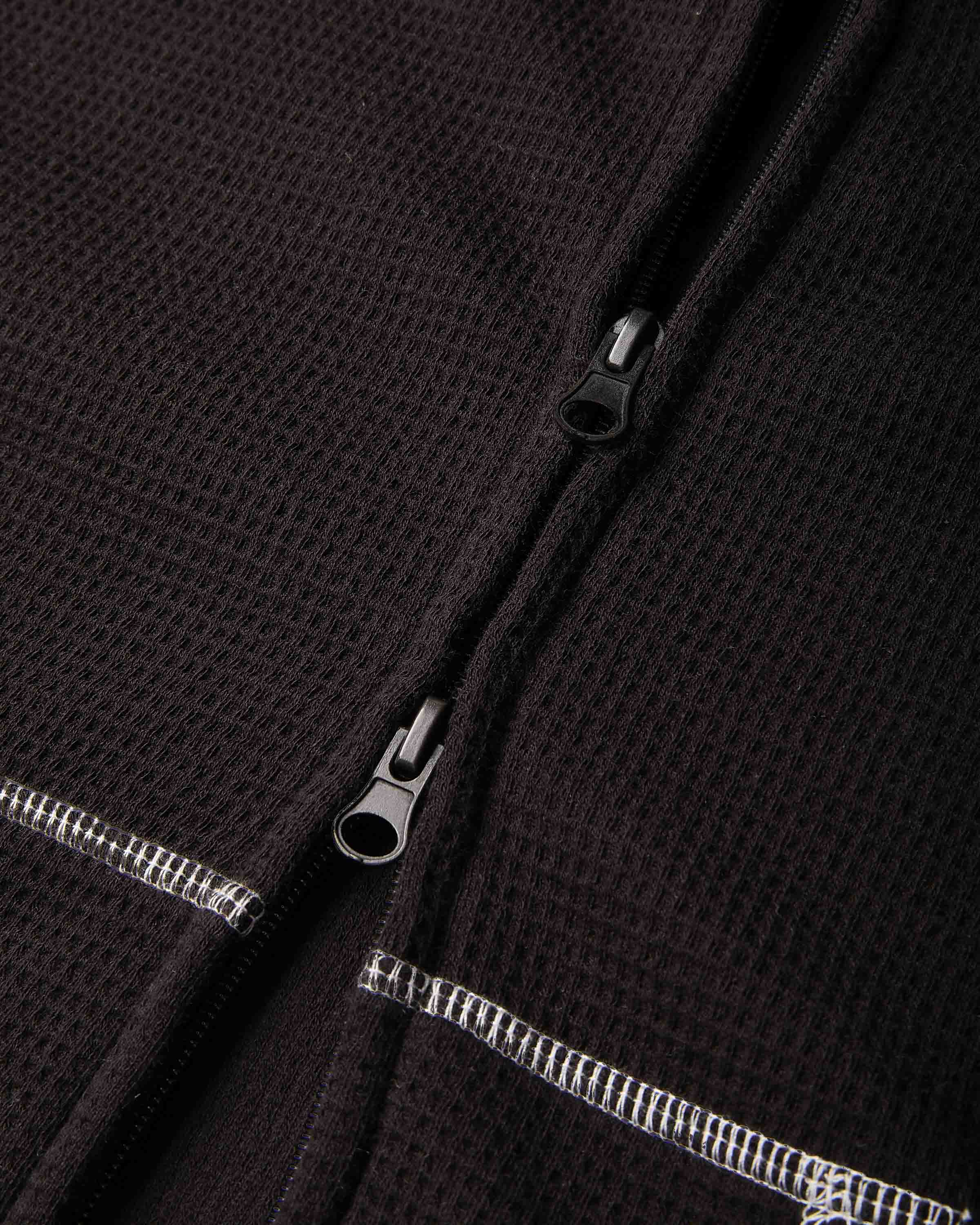 Close-up of a dark brown waffle-knit zippered garment, showing the textured fabric and silver-toned zipper pulls.