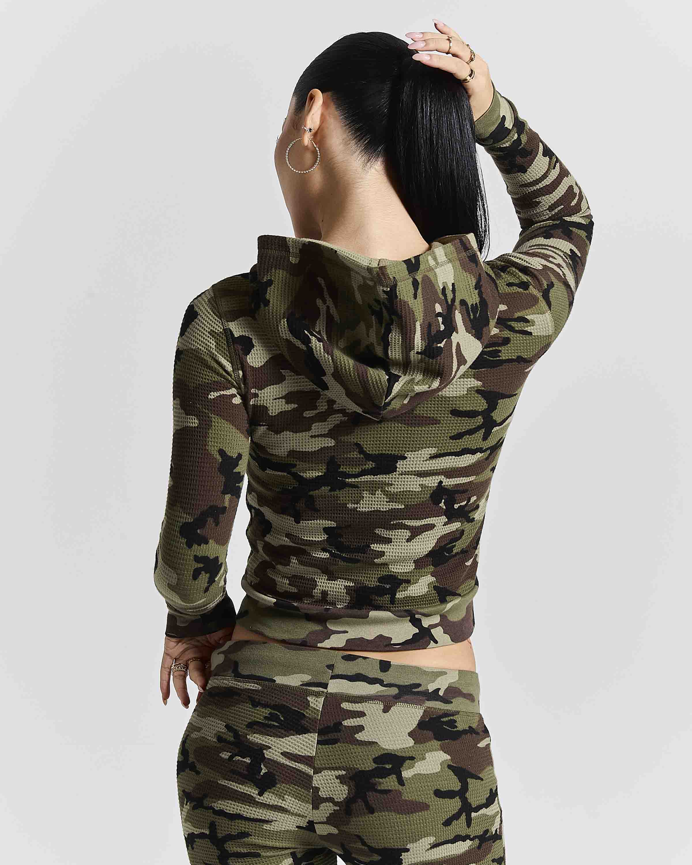 A woman shown from the back wearing a matching camouflage long-sleeve crop hoodie and high-waisted leggings set, against a light gray studio background.