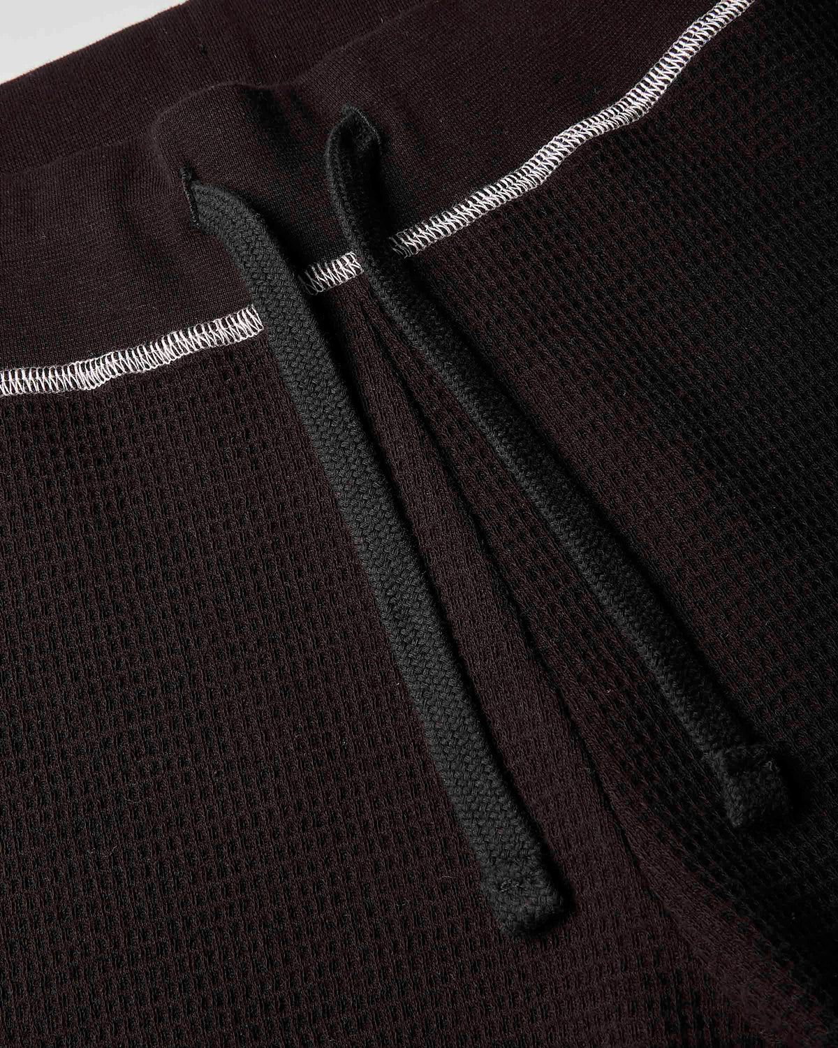 Close-up detail of a dark brown waffle-knit garment, showing a black drawstring and white contrast stitching.