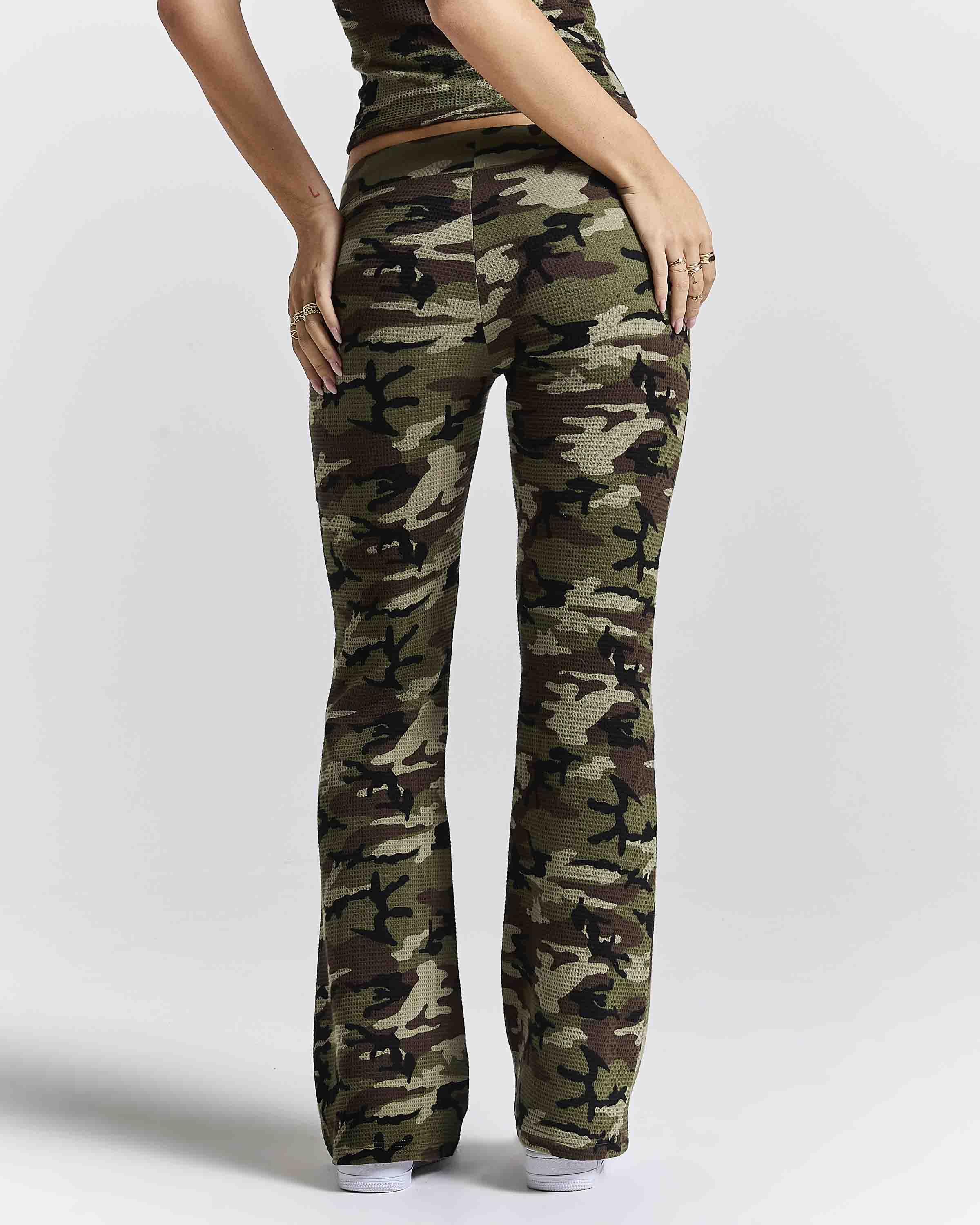 A person shown from the back wearing camouflage pants with a straight-to-flare leg, paired with a matching camouflage top against a light gray studio background.