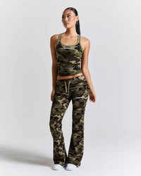 A woman modeling a matching camouflage athletic set consisting of a cropped tank top and high-waisted flared pants, photographed against a light gray studio background.