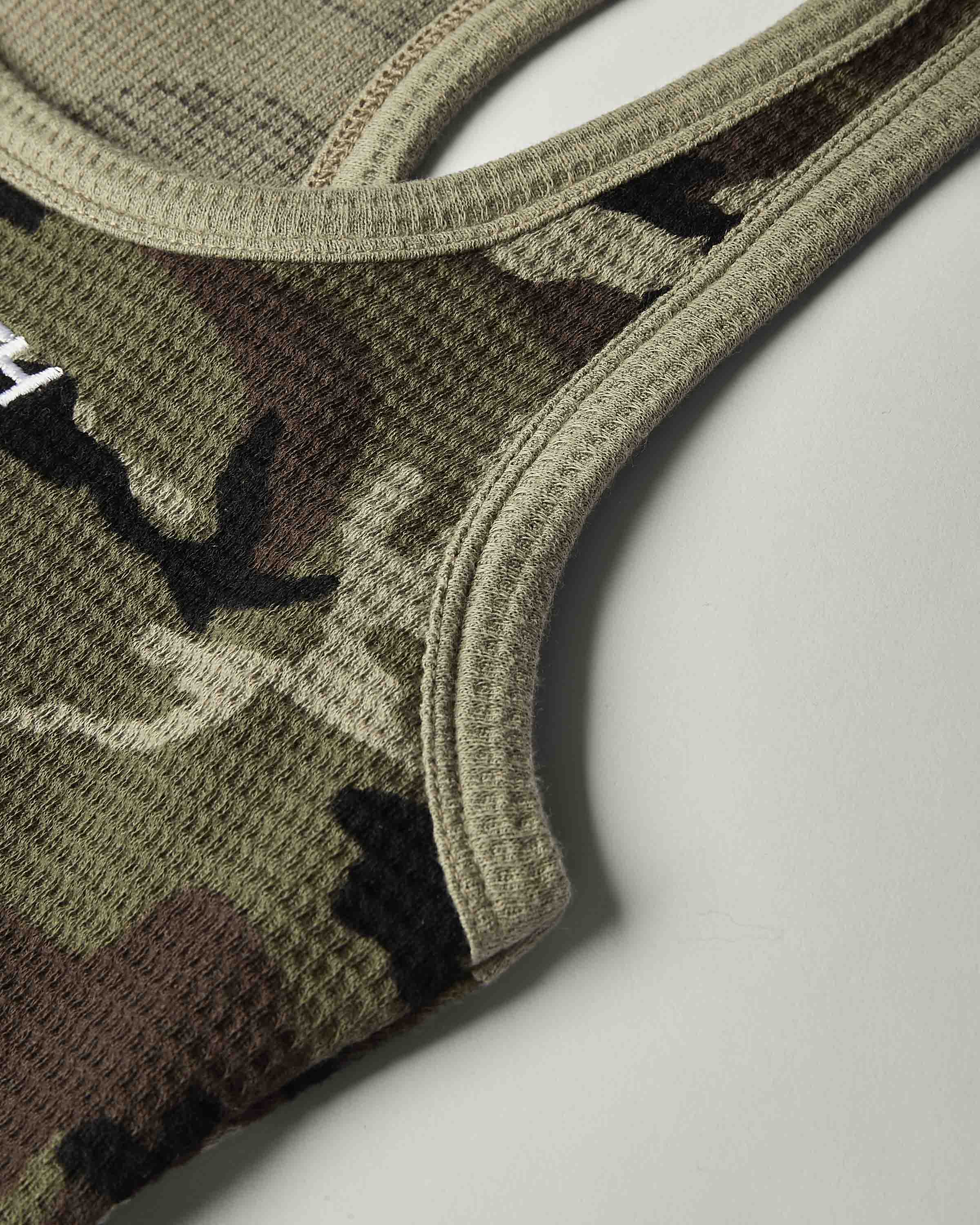 Close-up of a waffle-knit athletic top in a camouflage pattern, showing the textured fabric and ribbed trim on a light gray background.
