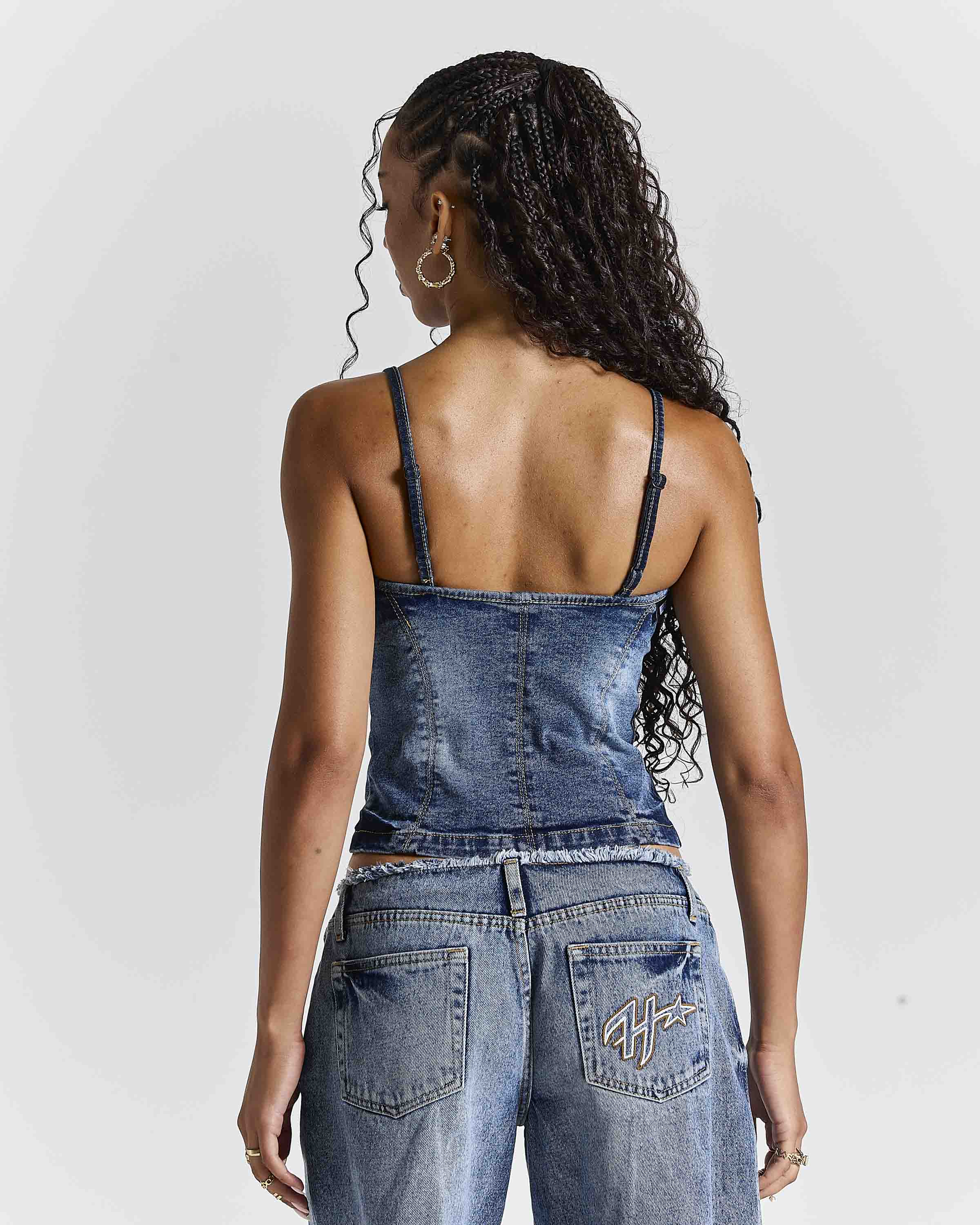 A woman shown from the back wearing a blue denim camisole top and matching denim pants against a light gray studio background.
