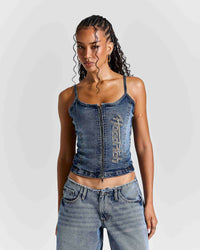 A woman modeling a cropped blue denim camisole top with a front zipper and vertical 'Hoodrich' text on the front, paired with light-wash jeans against a light gray studio background.