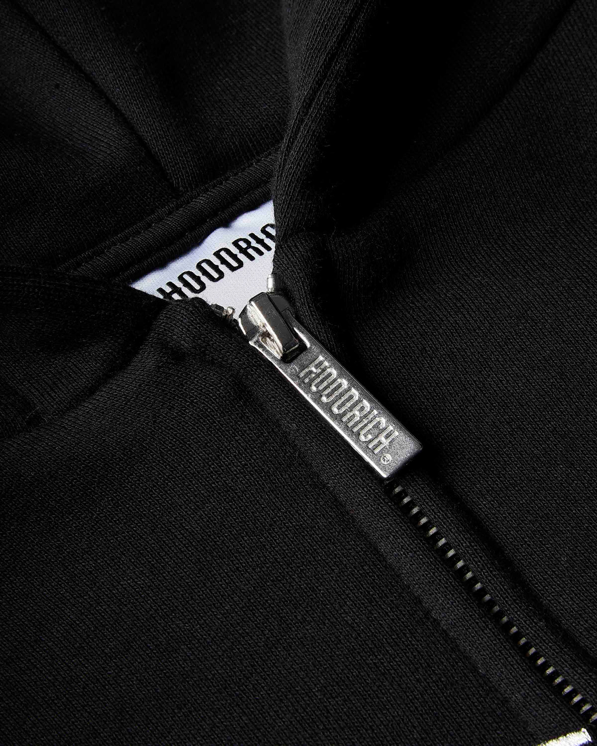Close-up of a black zip-up hoodie with a silver metal zipper pull engraved with the brand name 'HOODRICH'.