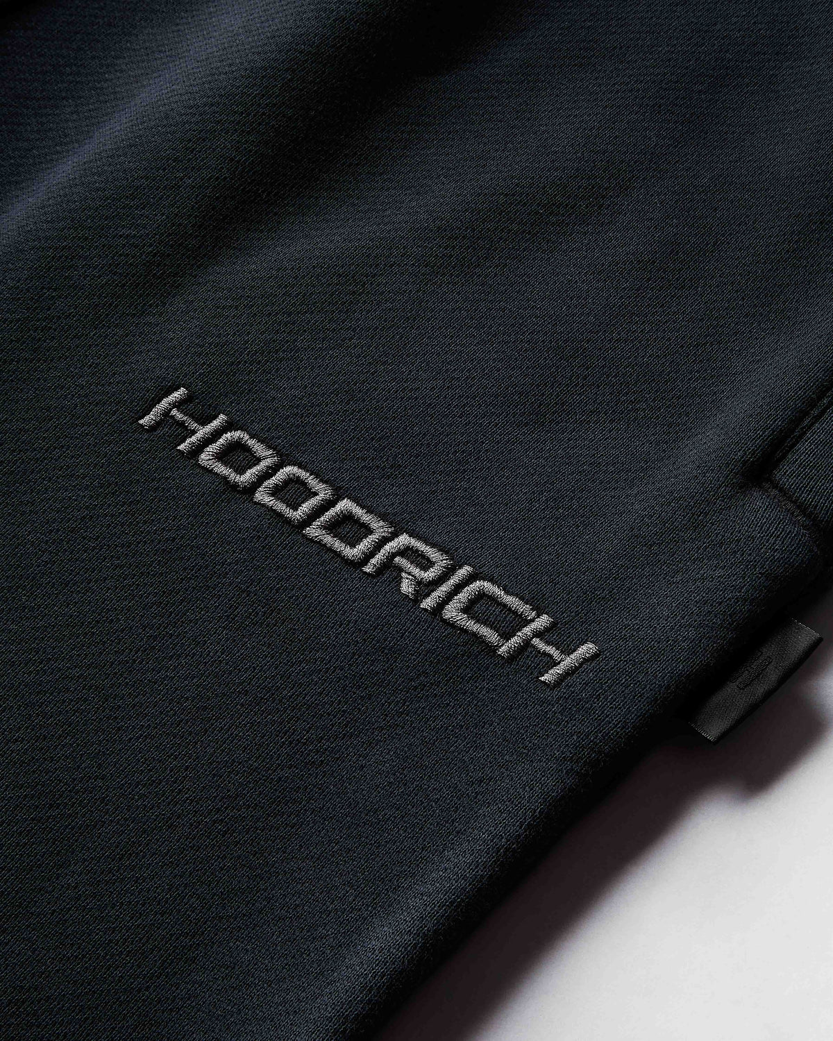 Close-up of a black jacket with 'Hoodrich' branding on a white background