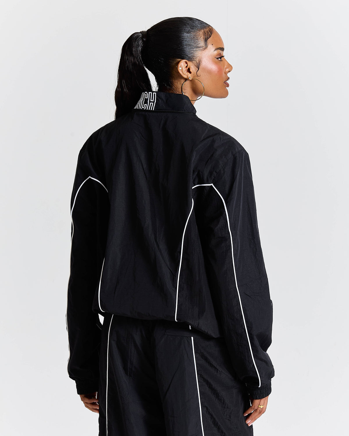 Person wearing a black tracksuit with white piping on a light gray background