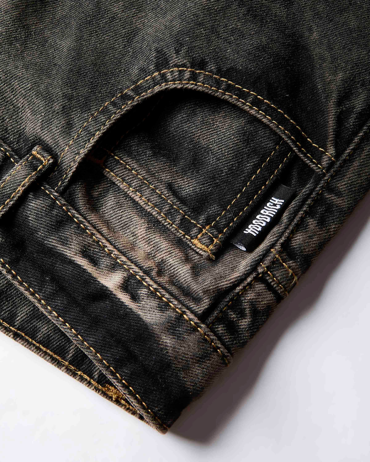 Close-up of a dark washed denim pair of jeans showing the back pocket with HOODRICH contrast stitching and a visible brand tag.