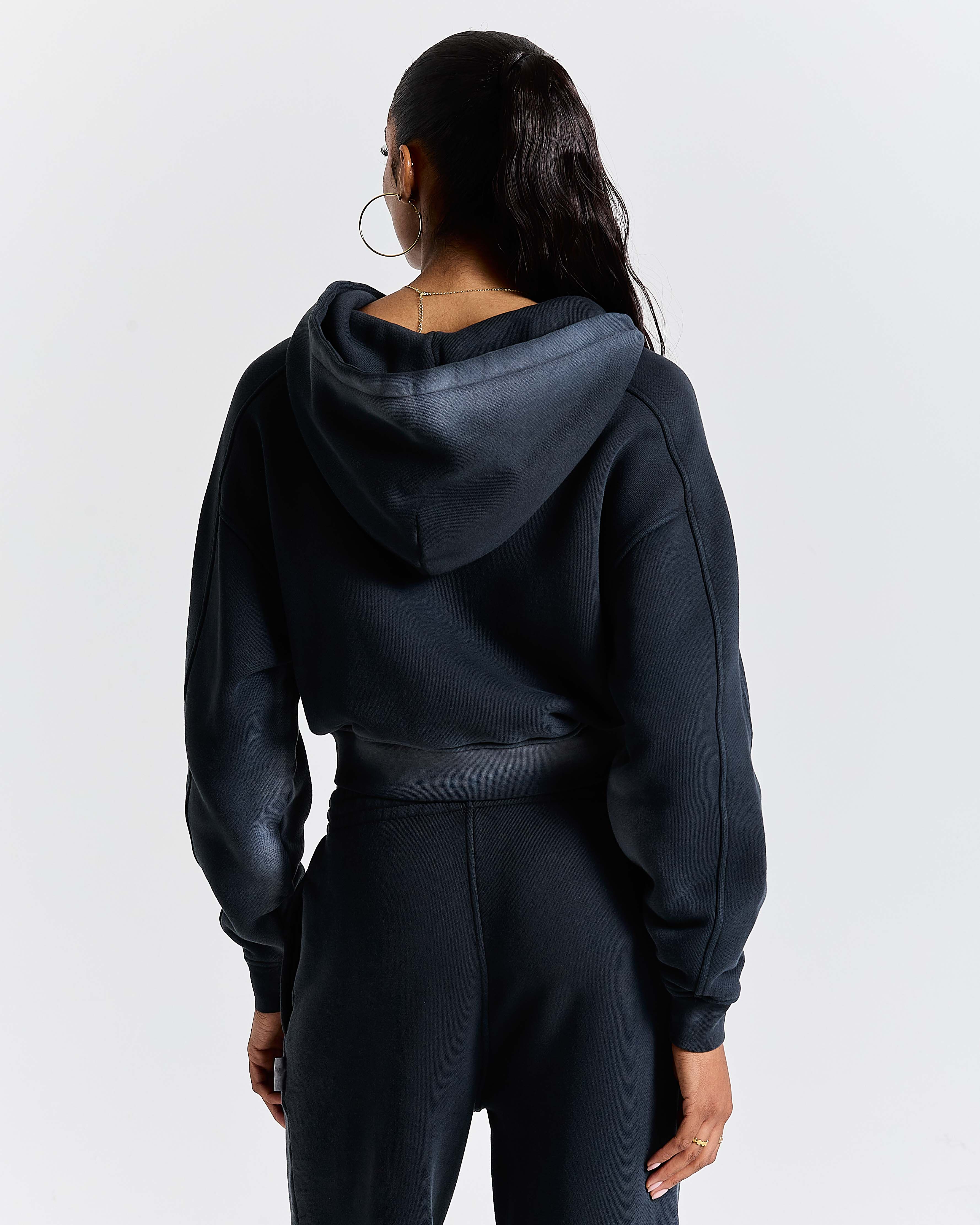Back view of a model wearing a black cropped zip-up hoodie.