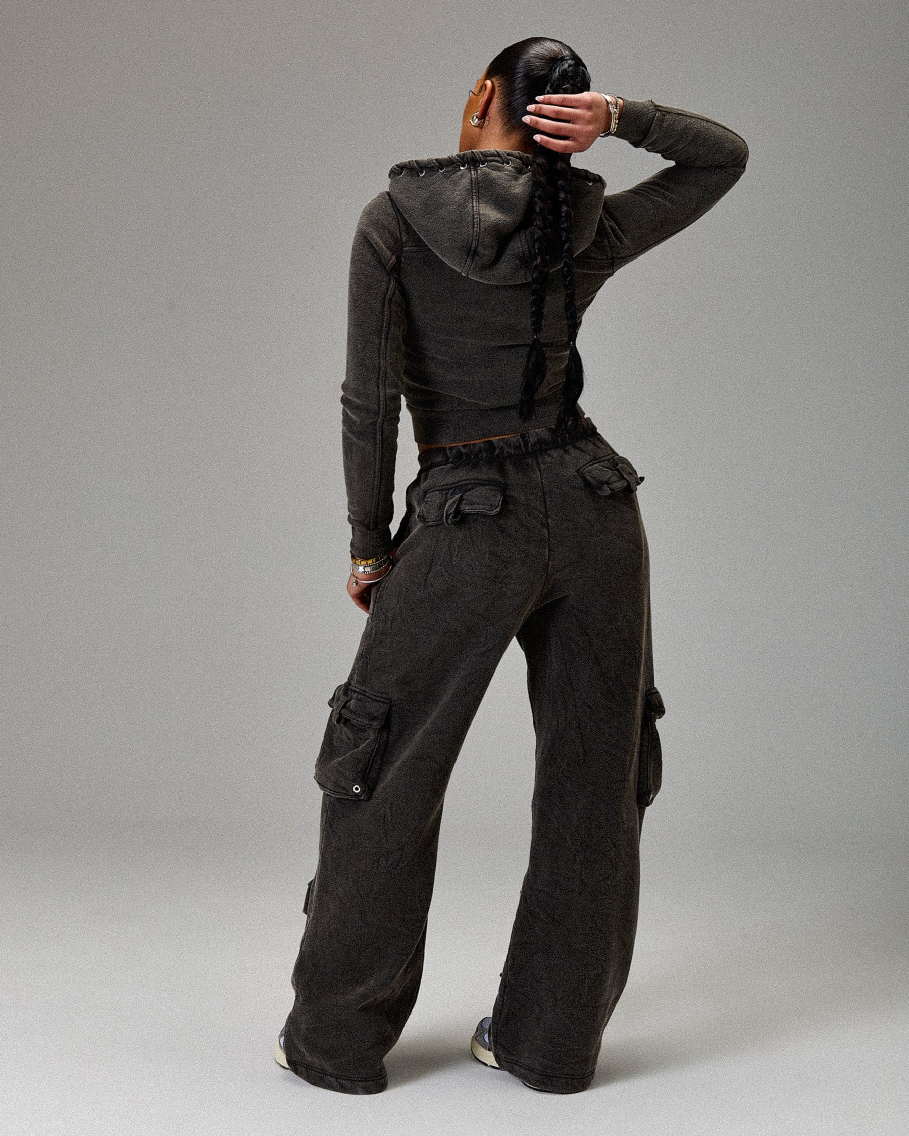 Person wearing a dark gray hoodie and cargo pants on a plain background