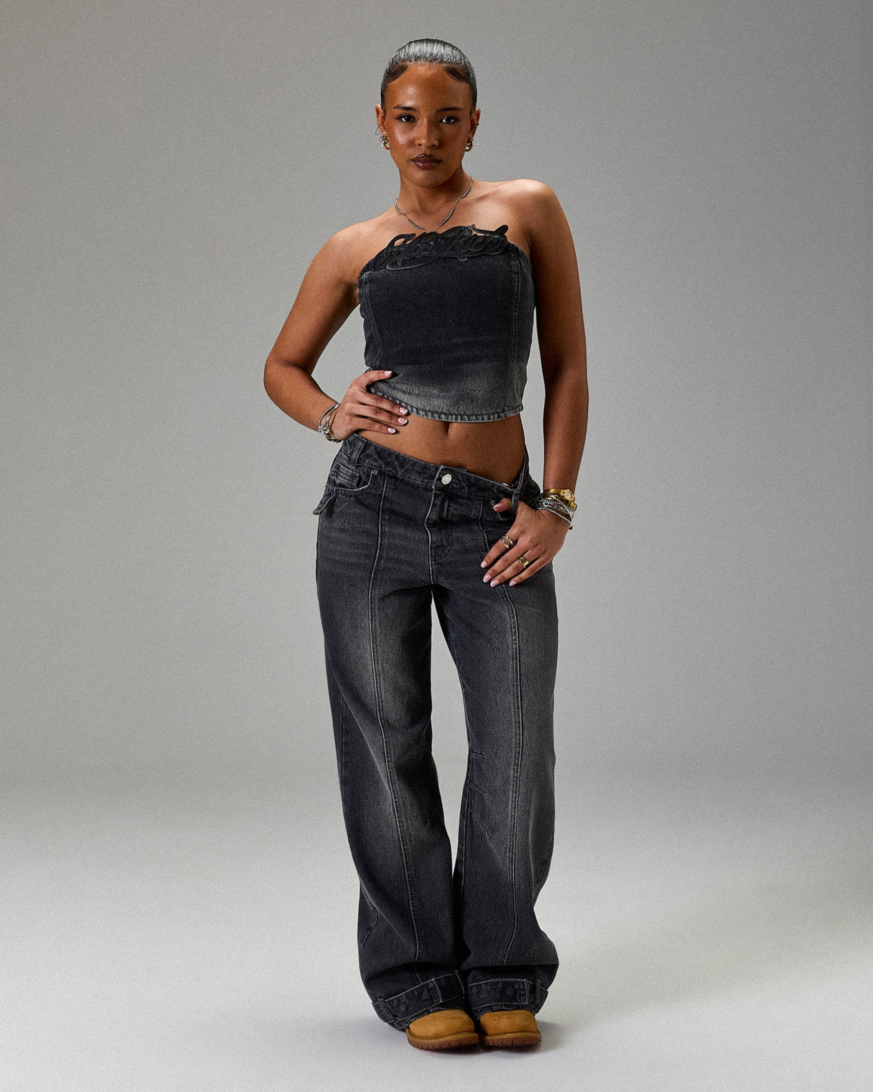 Woman wearing a black denim top and wide-leg jeans on a gray background