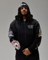 Person wearing a black zip hoodie with colorful designs on sleeves against a gray background